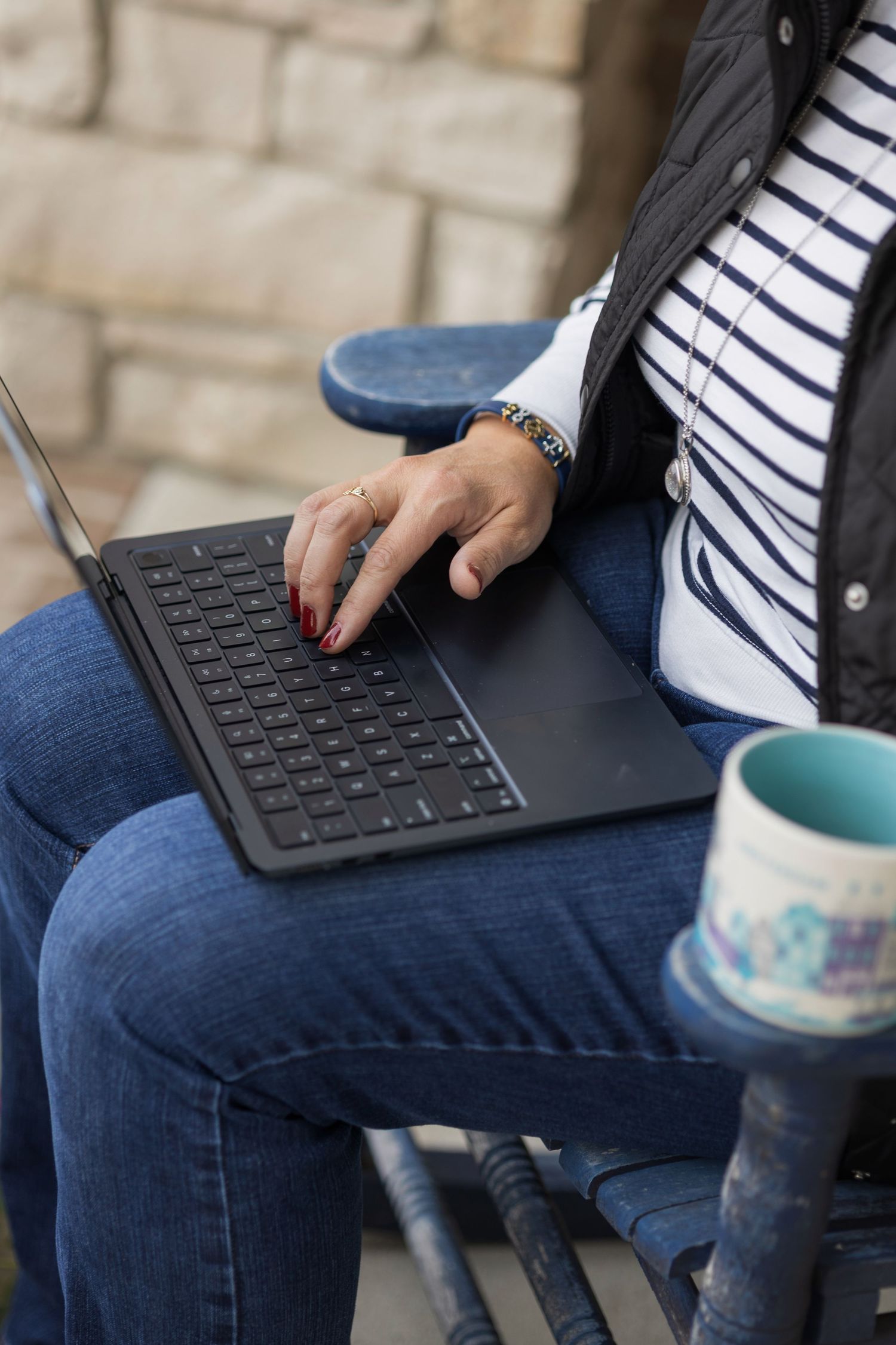 Person in striped shirt and jeans using keyboard while sitting with blue coffee mug nearby.