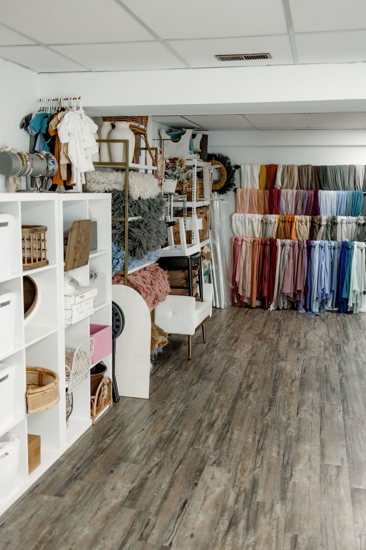 Modern retail store interior with wood flooring, white shelving units, and colorful clothing displays along the walls.