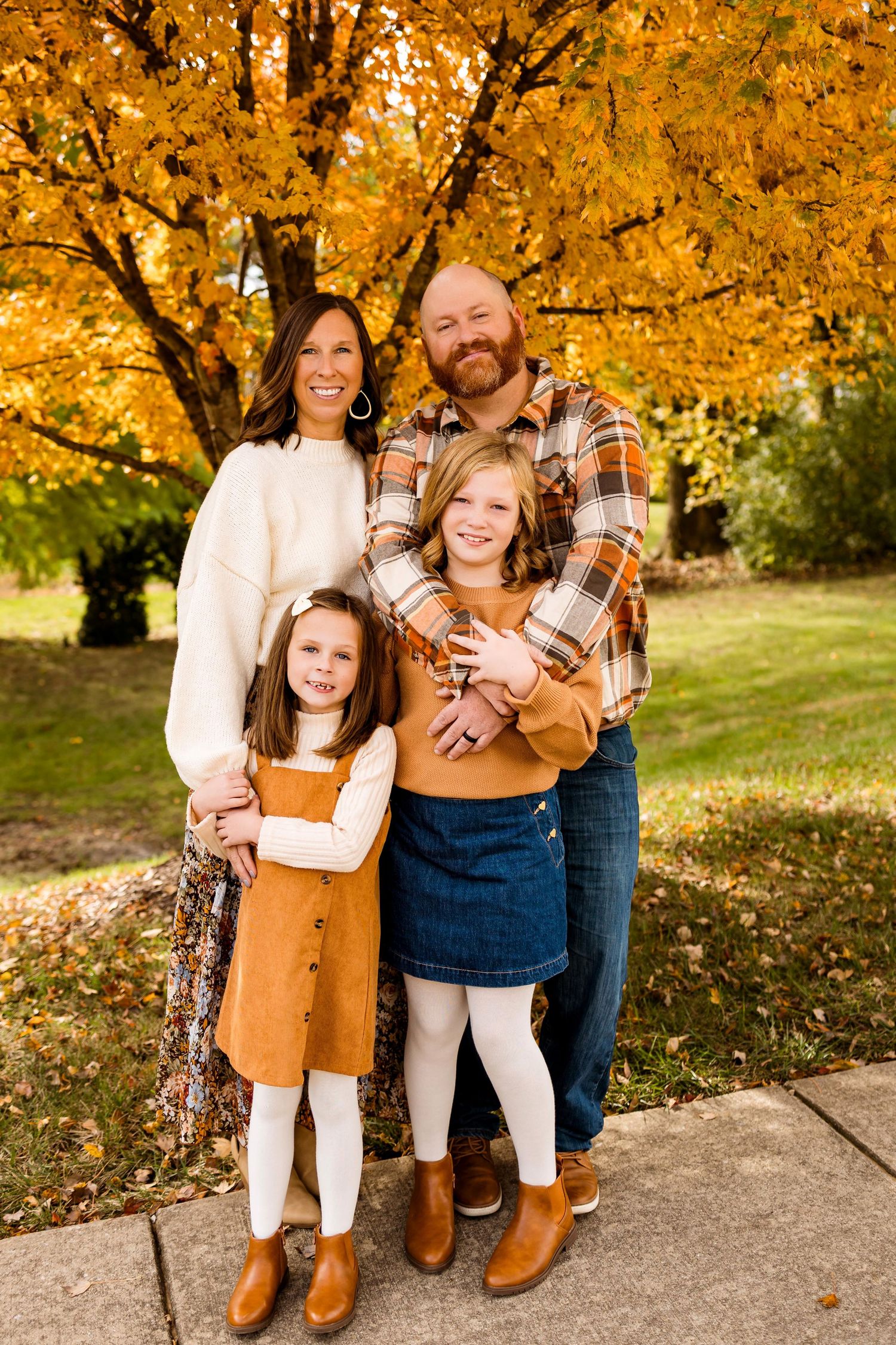 Family wearing coordinated fall outfits in orange and white poses together under golden autumn trees.