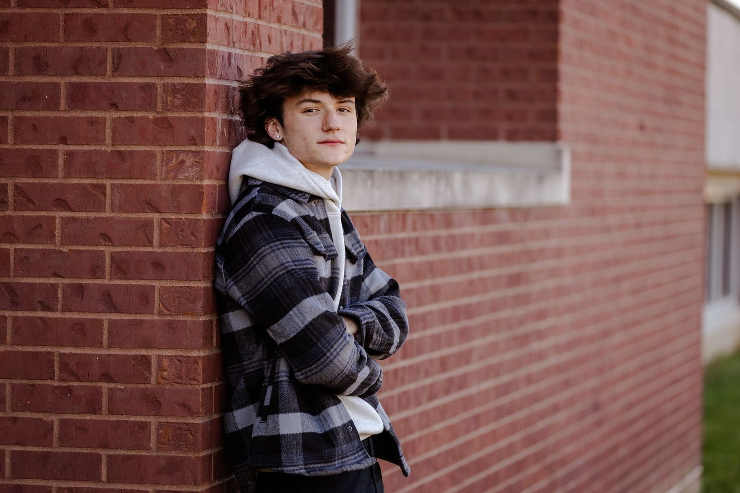 Person wearing striped hoodie leaning against brick wall outdoors.