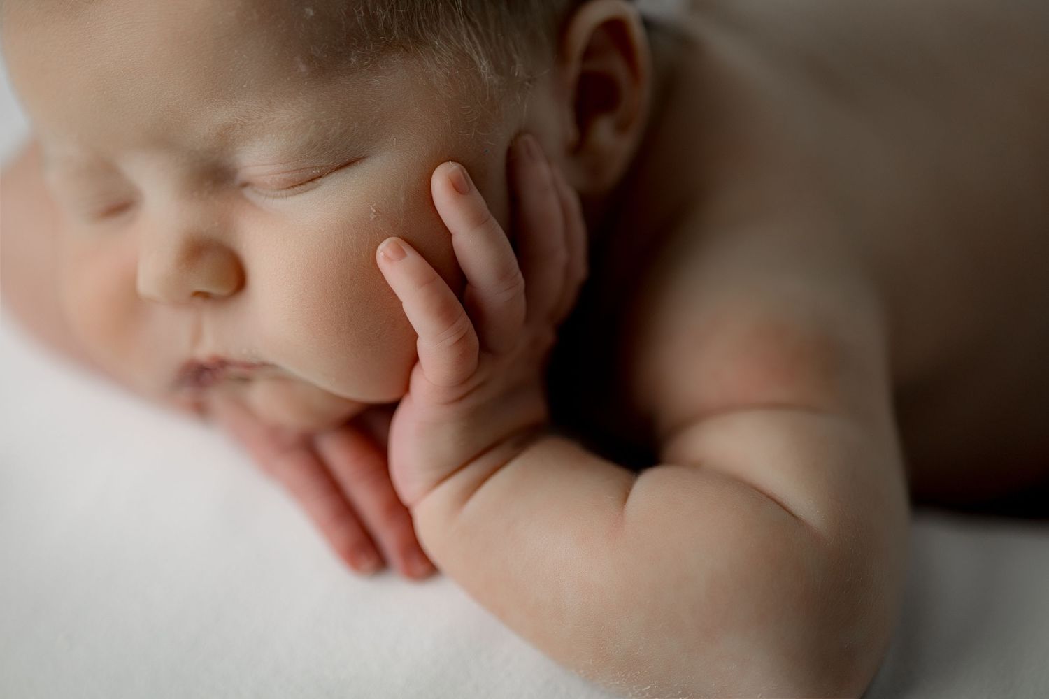 Peaceful newborn baby resting in gentle shadows with delicate features highlighted.