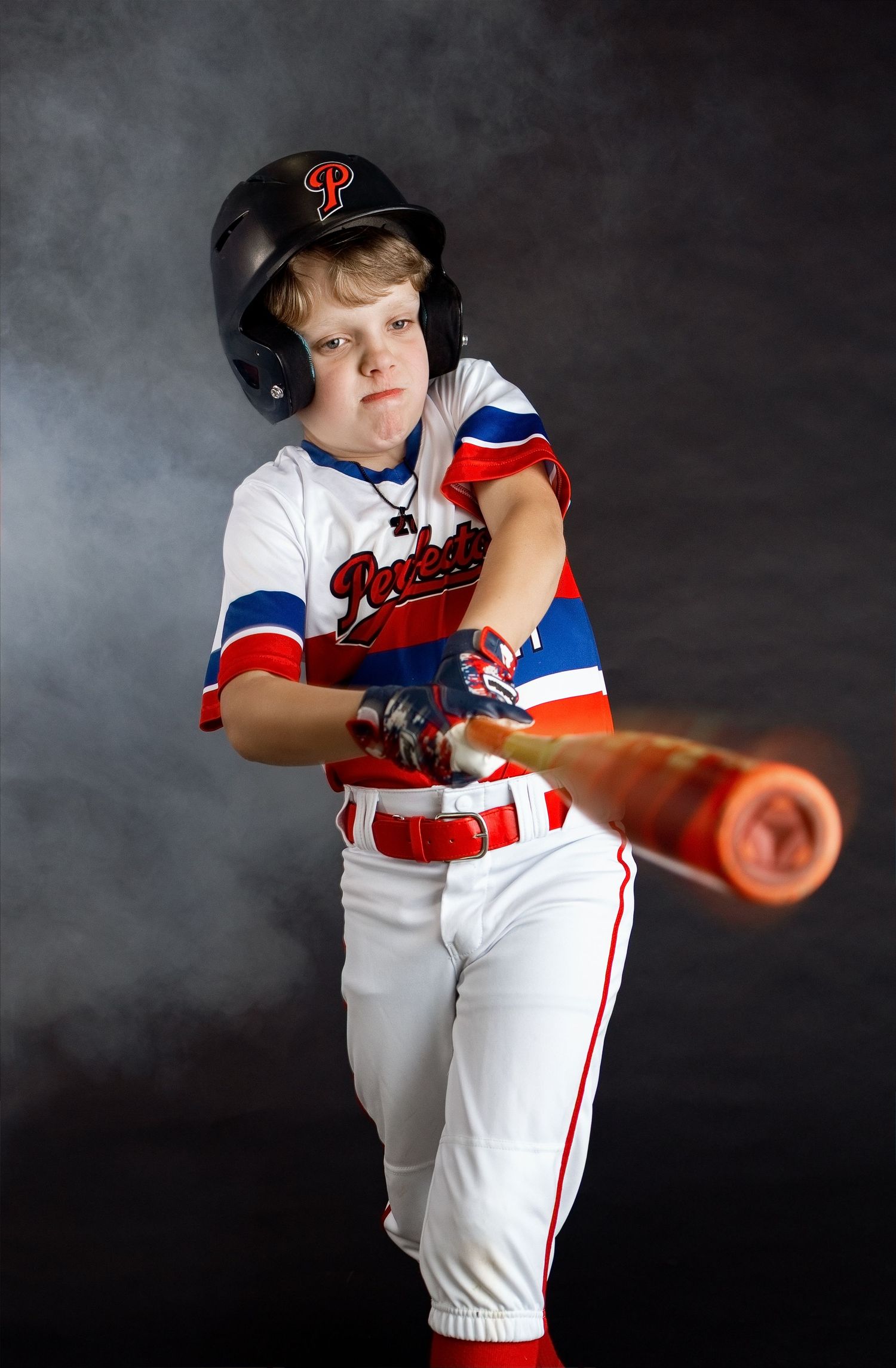 Young baseball player swinging a bat against a dramatic smoke backdrop during an Edwardsville milestone session