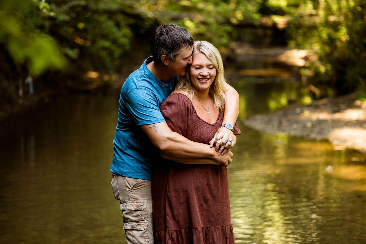 A family shares joyful moments together while playing in a serene creek surrounded by trees and sunlight.