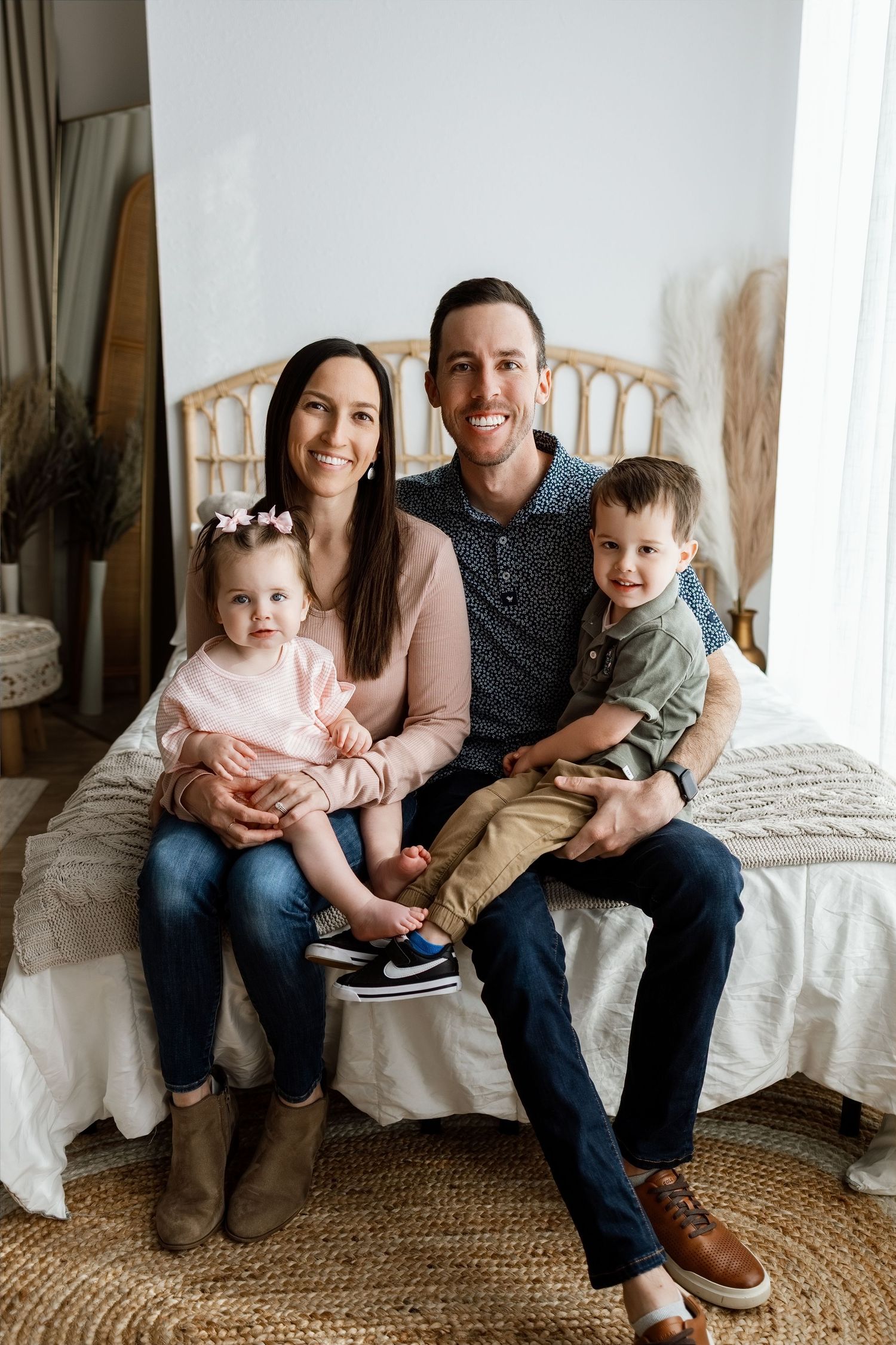 Family of four smiling together on the studio bed during a baby’s first-birthday photography session in Edwardsville