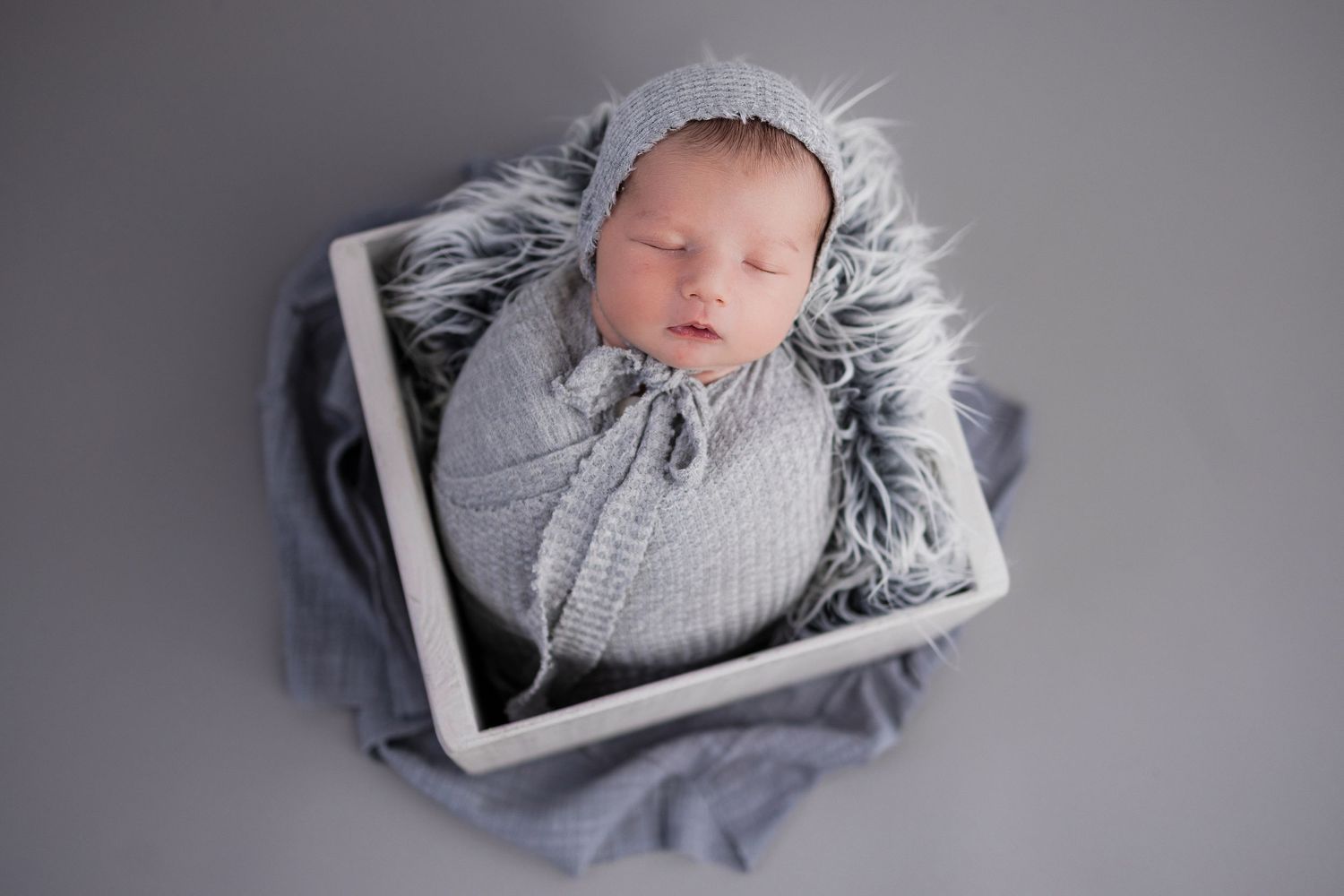 Seven monochromatic baby photos showing a sleeping newborn wrapped in gray textiles and posed in various positions.