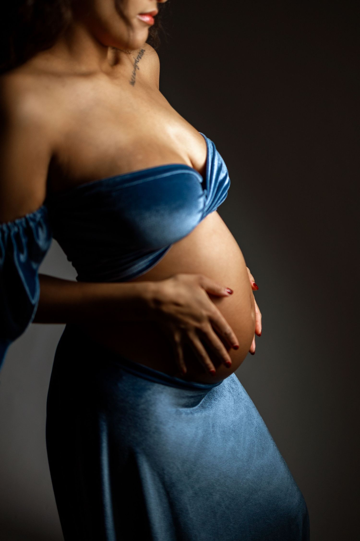 Artistic maternity photography series showing pregnant belly in blue dress against dark background.