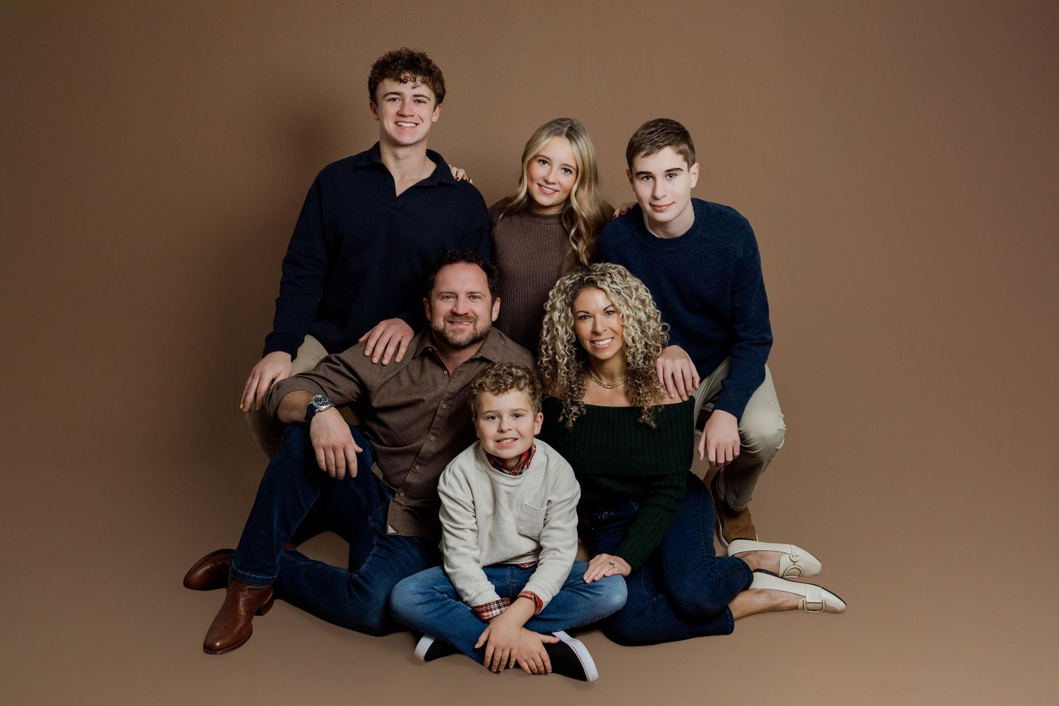 A family wearing coordinated blue and brown outfits poses together for a professional portrait session.