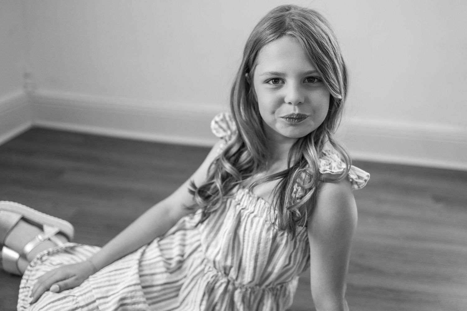 Black and white portrait of a young person in a light sleeveless dress sitting on the floor.