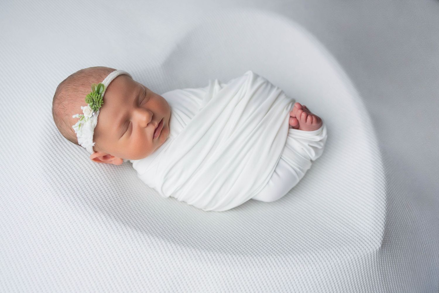 Minimalist newborn photography setup with white fabric and curved posing surface.