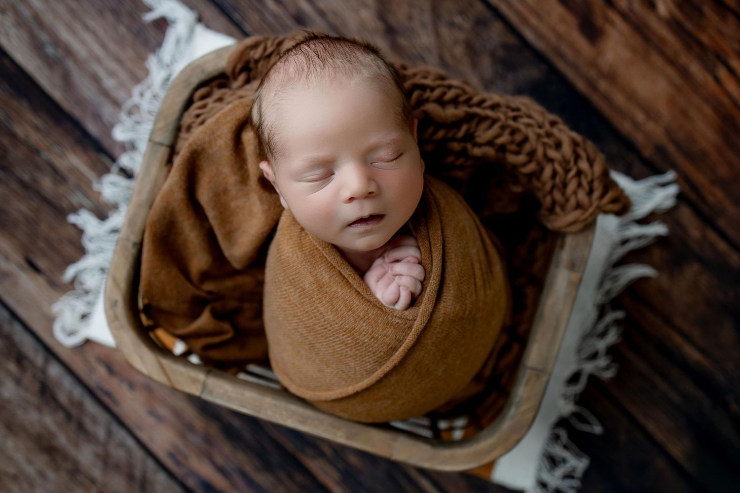Artistic newborn photography series featuring brown swaddle blankets and rustic wooden backdrop with delicate floral accents.