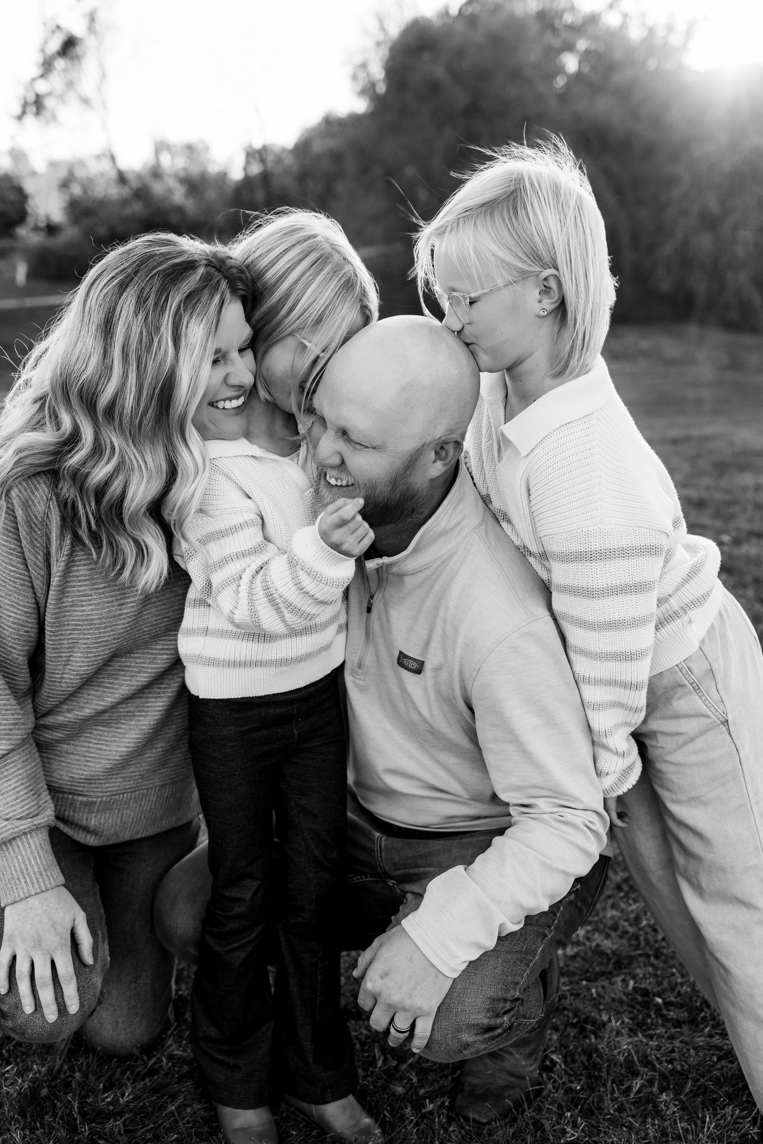 A family shares a joyful moment together outdoors in black and white, laughing and embracing on the grass.
