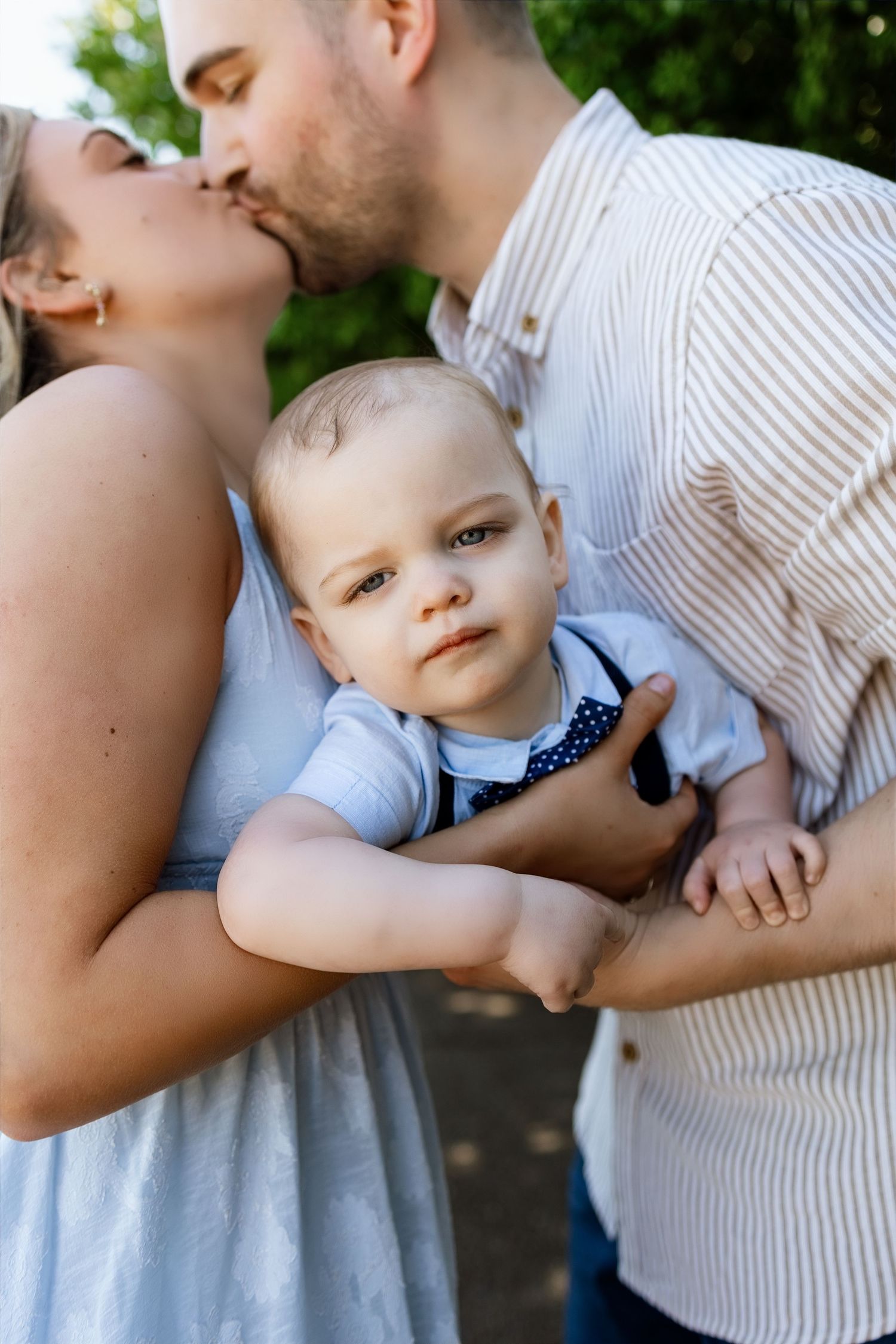 Parents sharing a kiss while holding their baby during an outdoor family photography session near Edwardsville