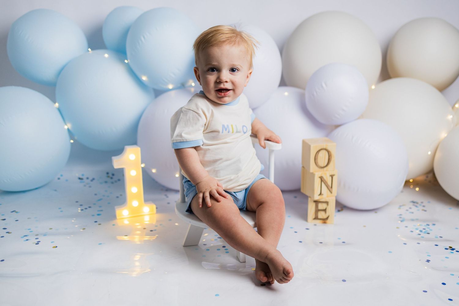 Blue and white balloon decorations create a festive first birthday celebration scene with glowing number candles.