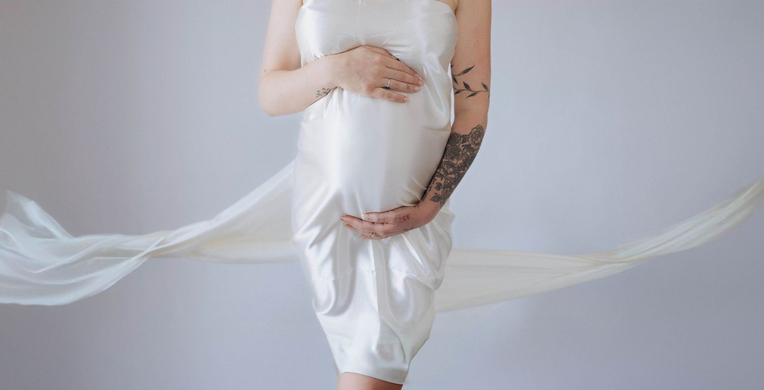 Ethereal maternity portrait series in white fabric against a grey backdrop, capturing gentle flowing movement and curves.