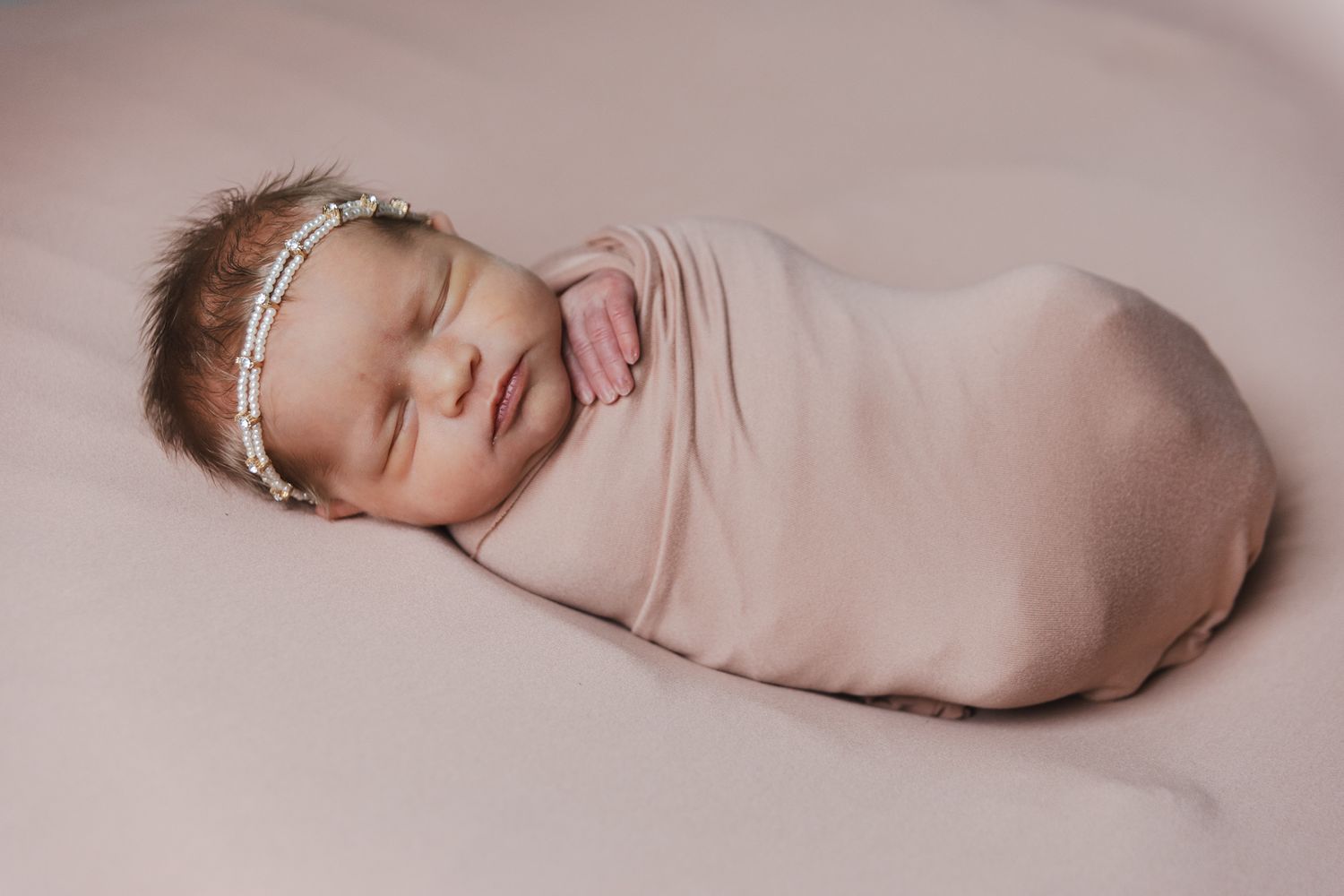 Sleeping newborn baby wrapped in soft pink swaddle wearing delicate headband.