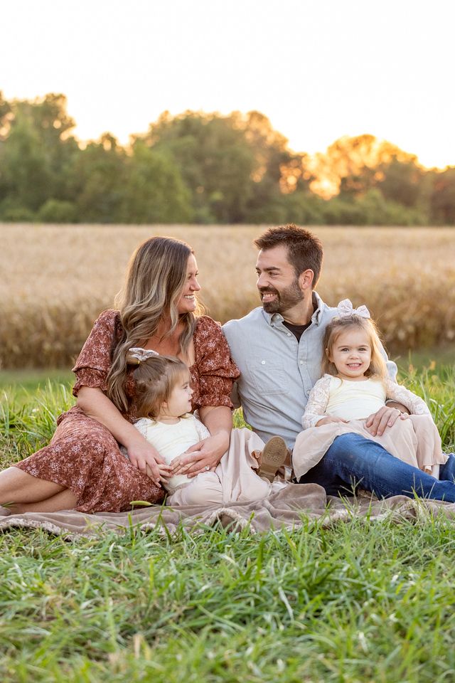 A family lying together in a grassy field at sunset enjoying a tender moment in nature.