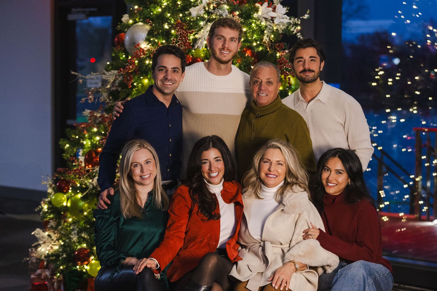 Group photo of friends gathered in front of decorated Christmas tree with lights.