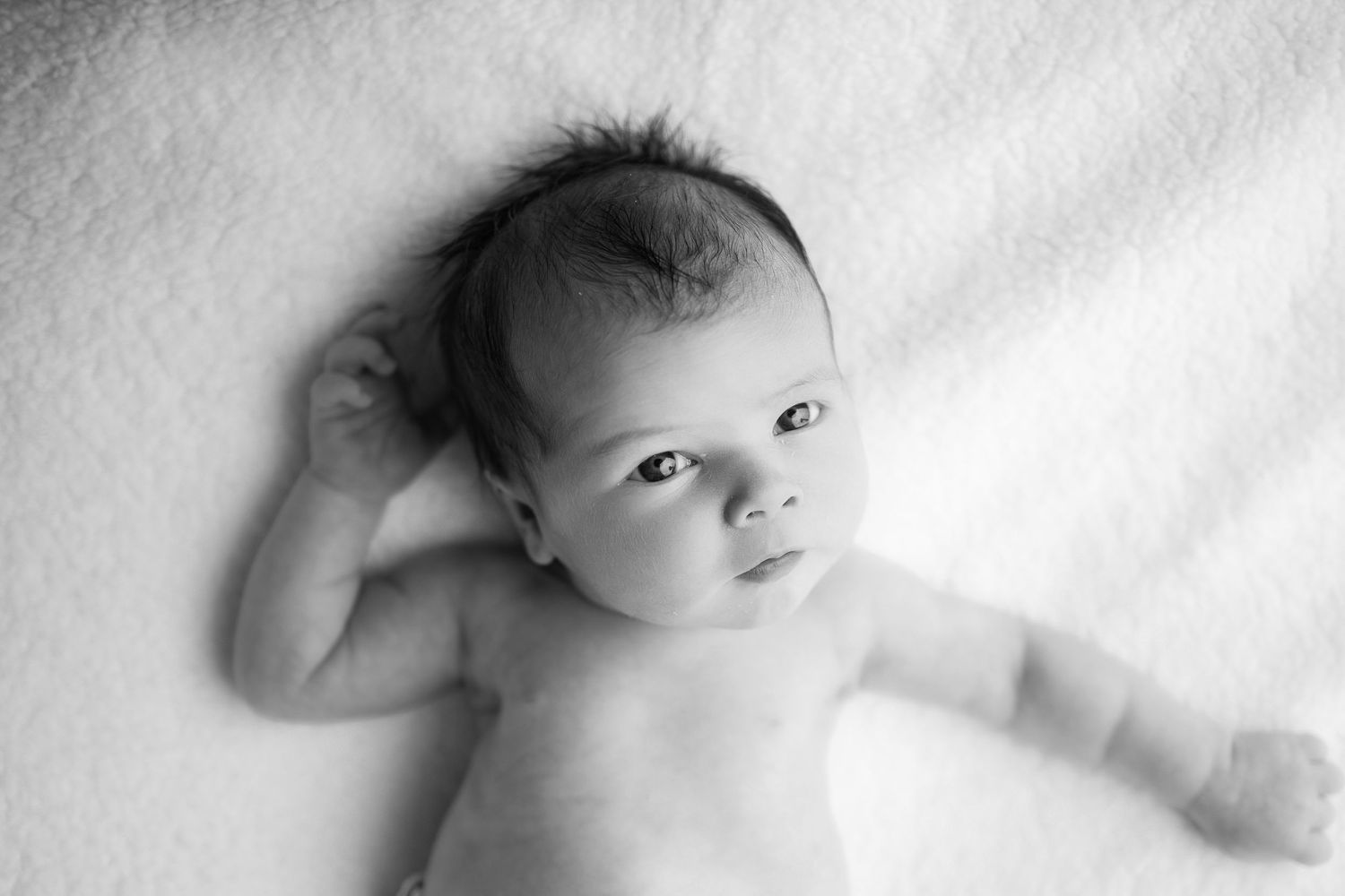 Black and white portrait of newborn lying on white blanket.