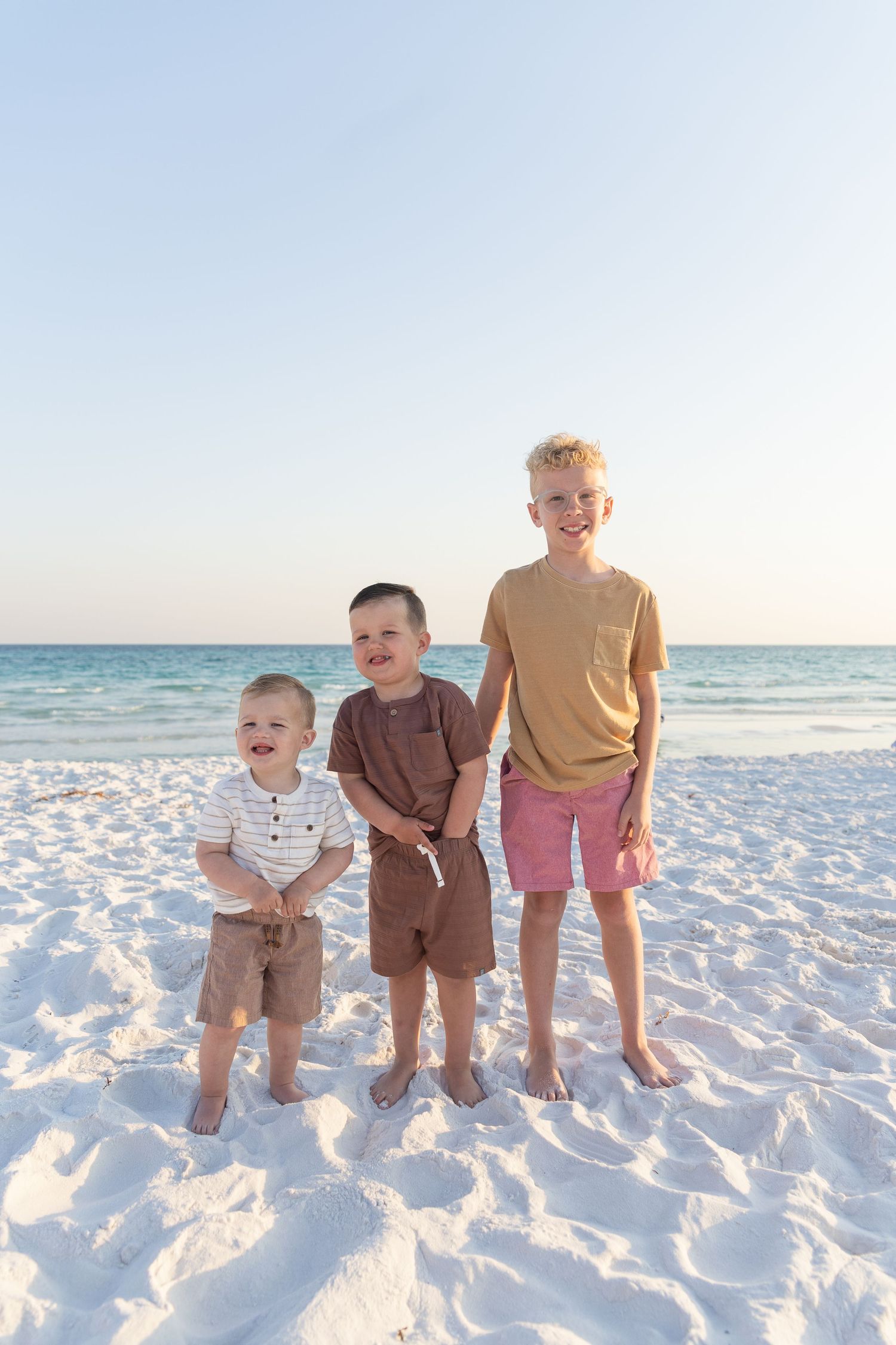 Three children standing together on pristine white beach.
