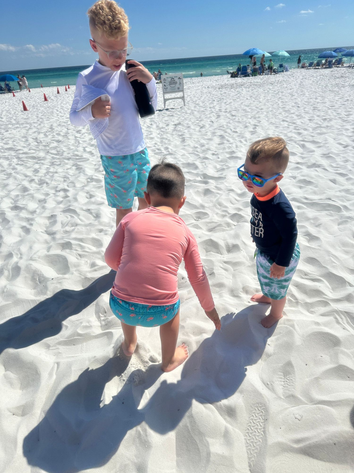 Children playing on pristine white sand beach with beach umbrellas in background.