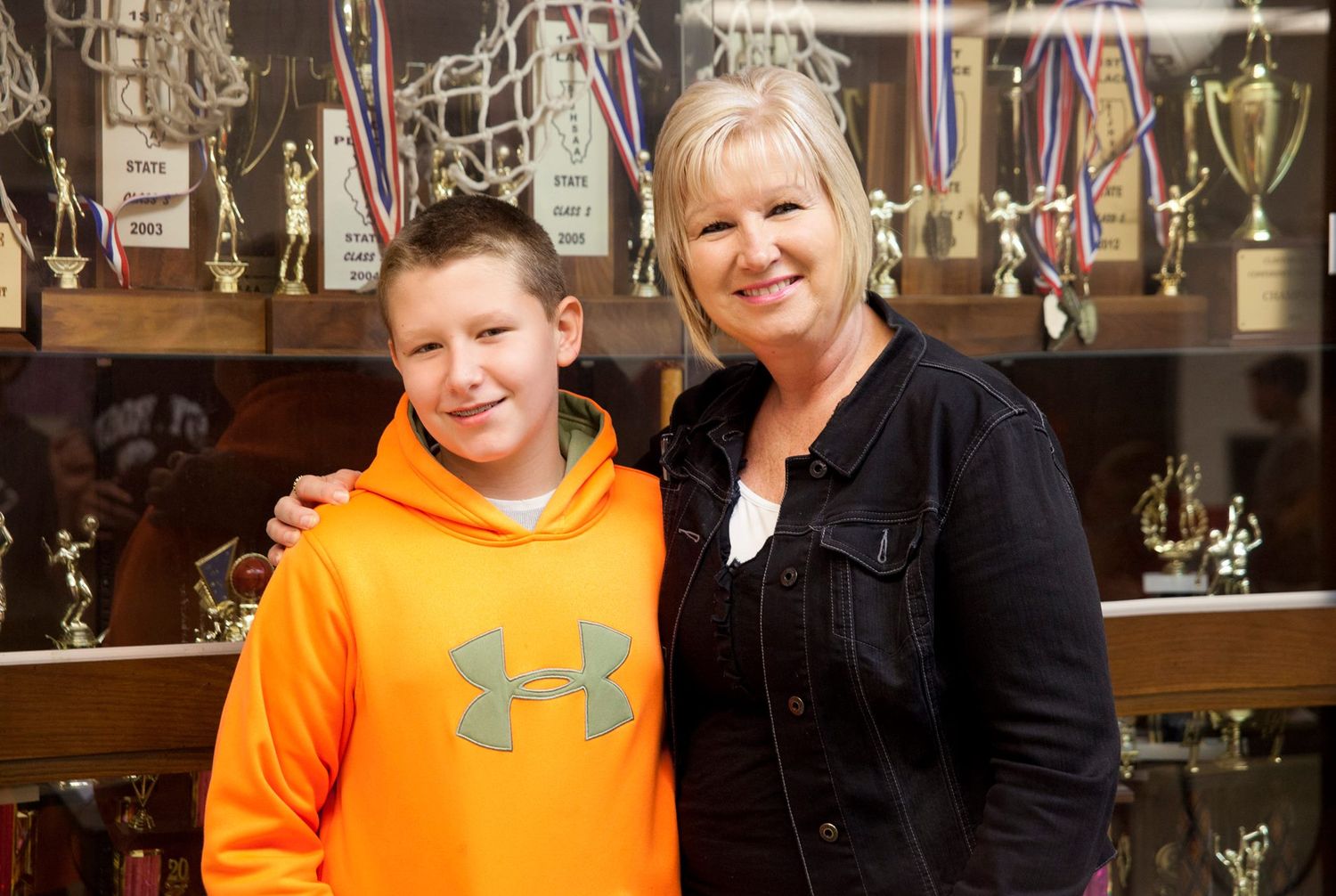 Heartwarming moment with trophy display cabinet showing athletic achievements in background.
