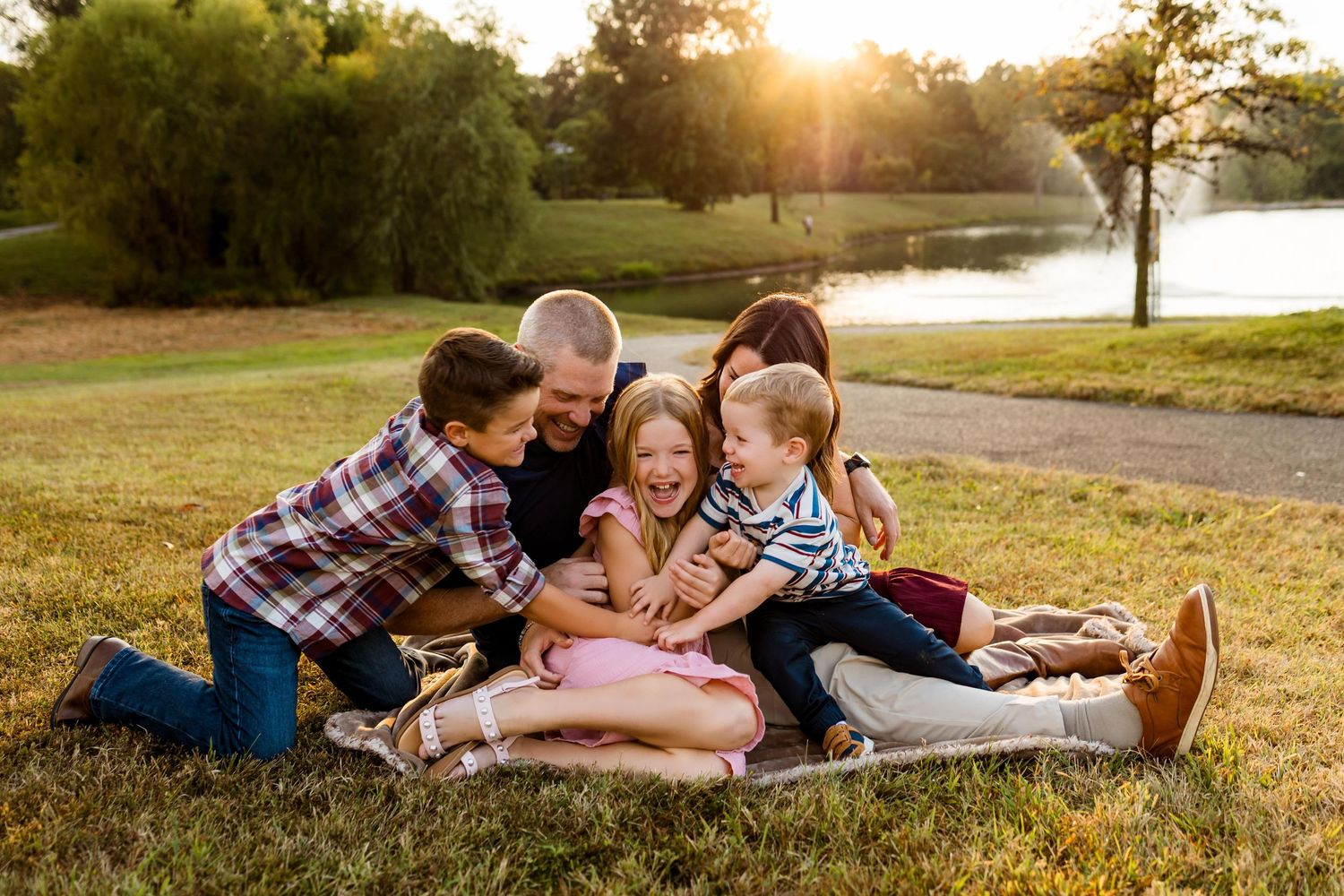 Family laying together on blanket in grassy field during golden sunset hour.
