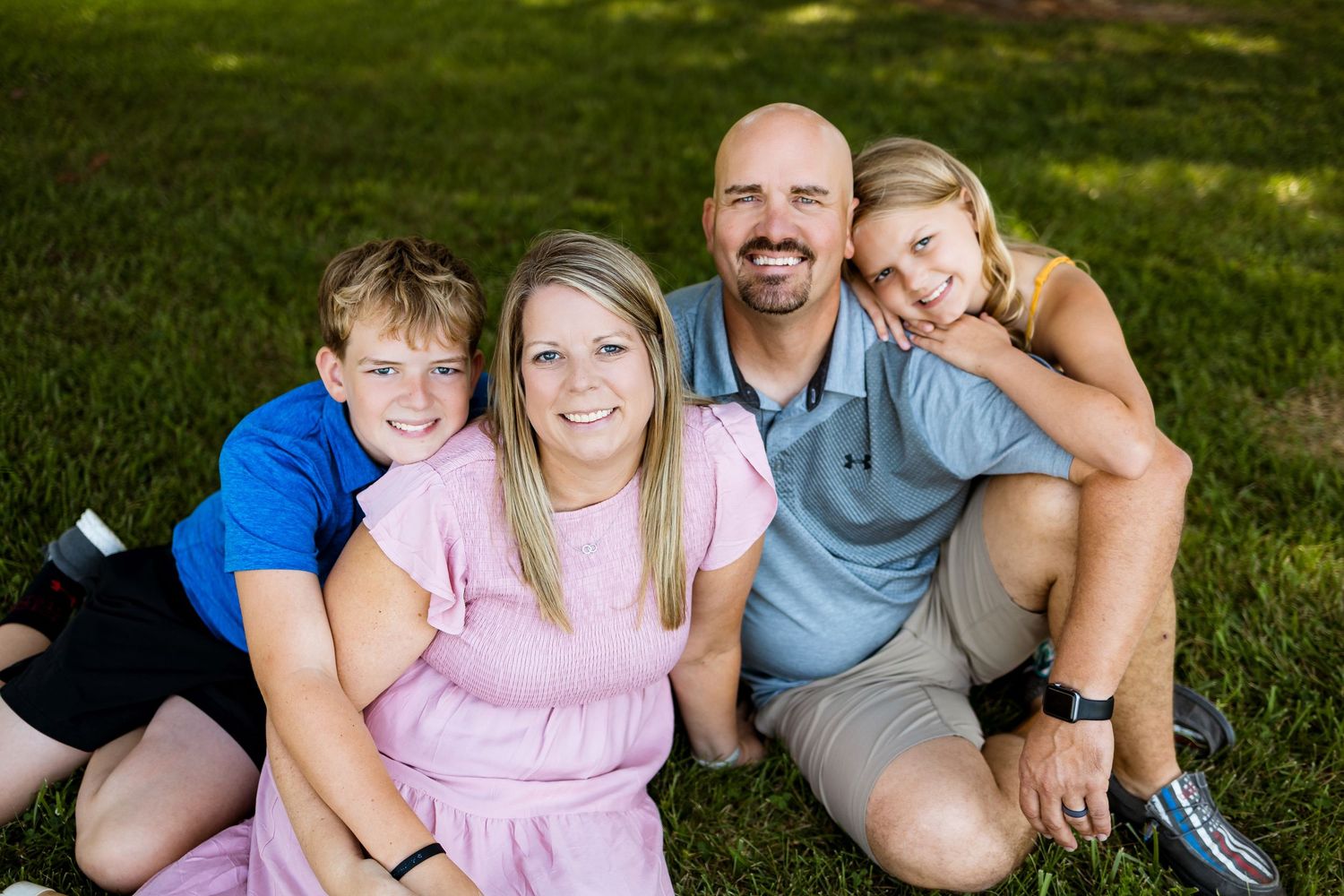 Candid family photo session outdoors with people sitting on grass in coordinated outfits on a sunny day.