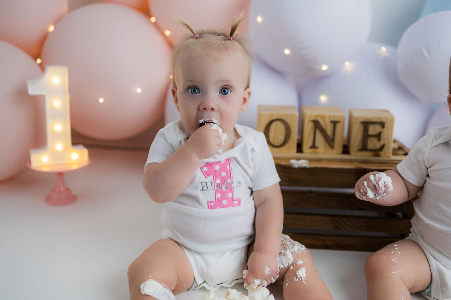 Pink and gold themed first birthday party decorations with balloons, lights, and cake set up for a special celebration.
