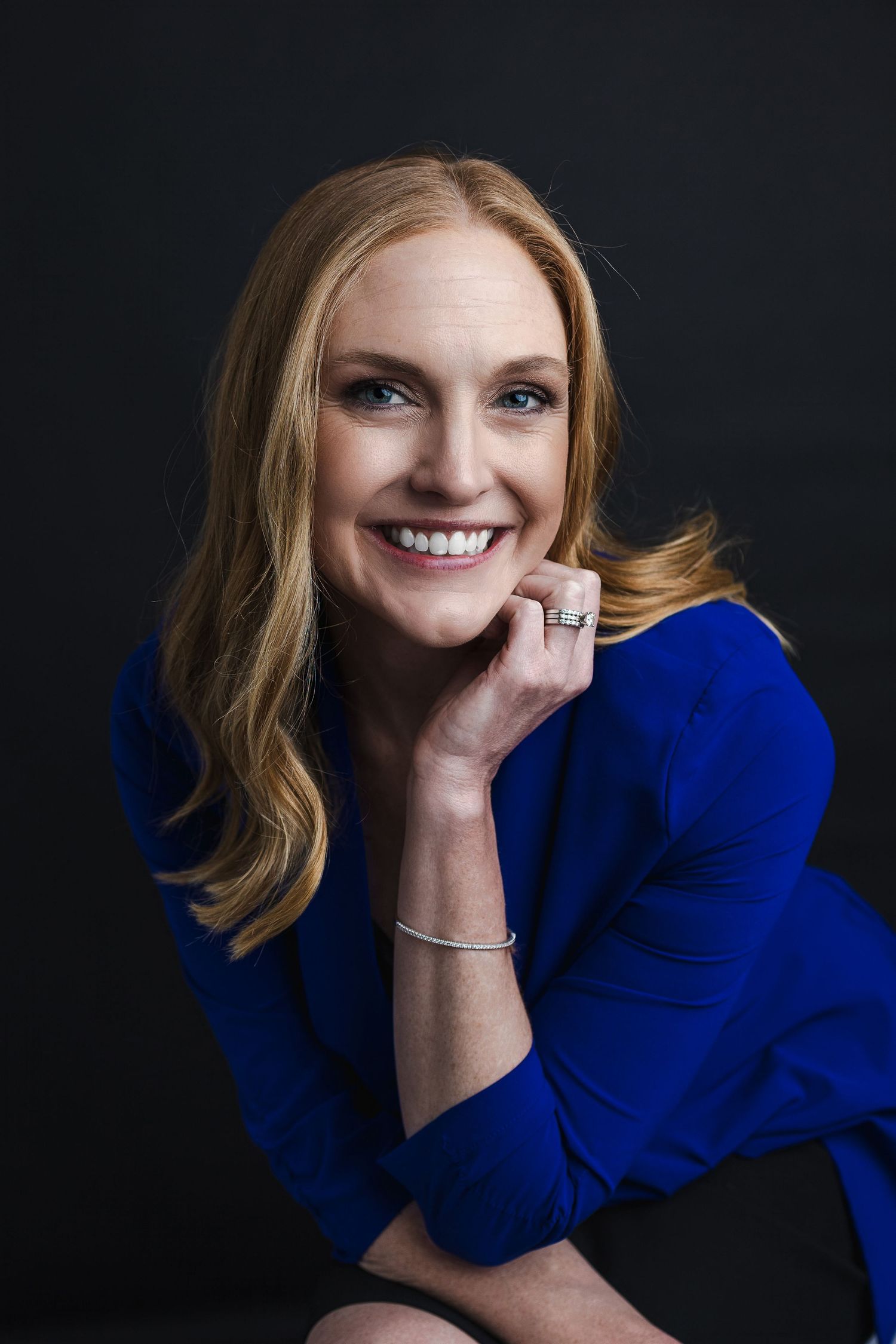 Professional portrait of person in royal blue sweater against dark background.