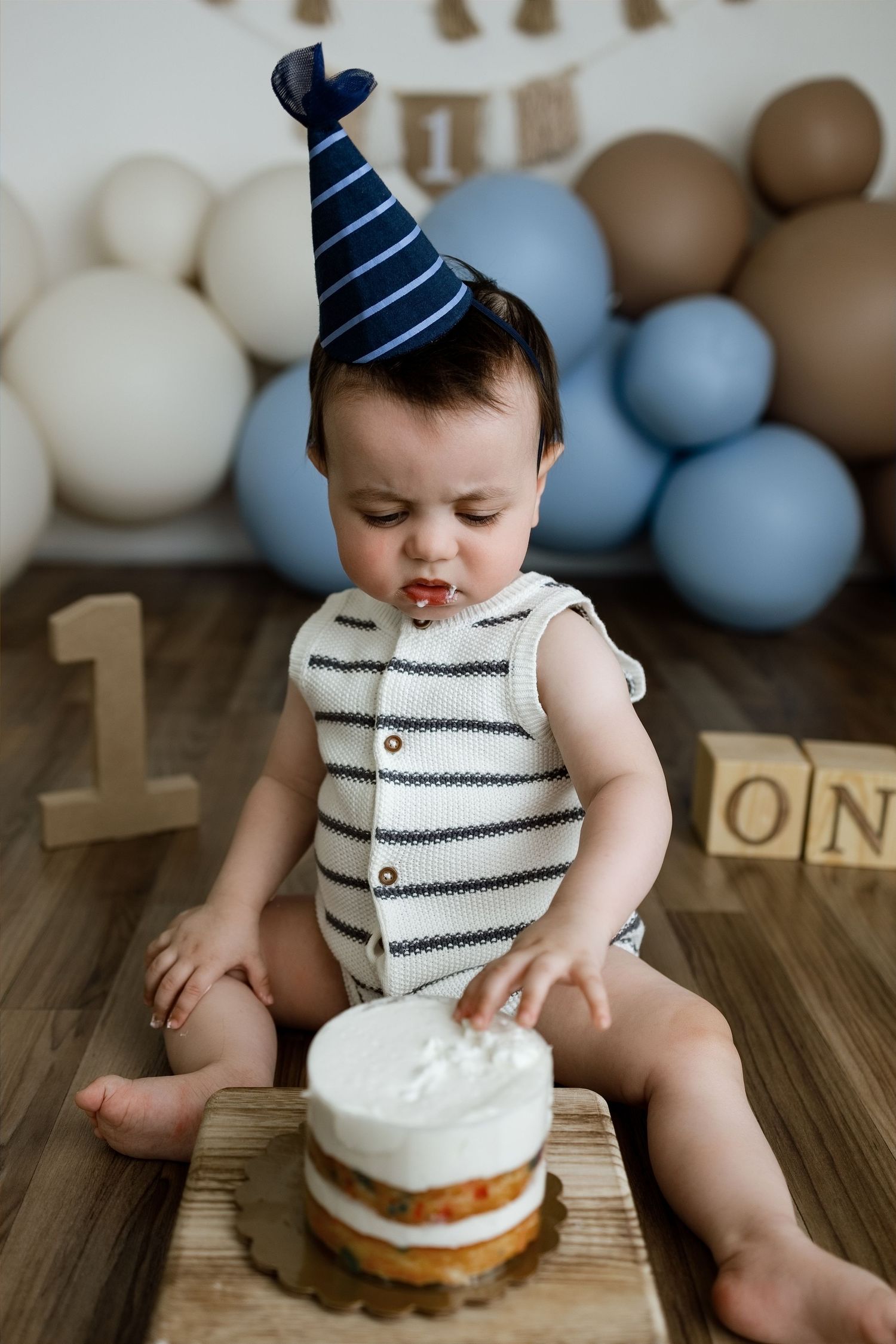One-year-old boy wearing a party hat and touching his cake during an Edwardsville cake smash photography session
