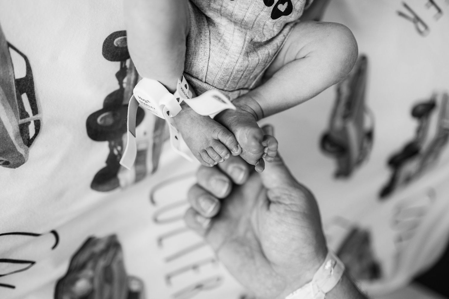 Close up black and white image showing a baby's feet and hands being gently held against a patterned background.