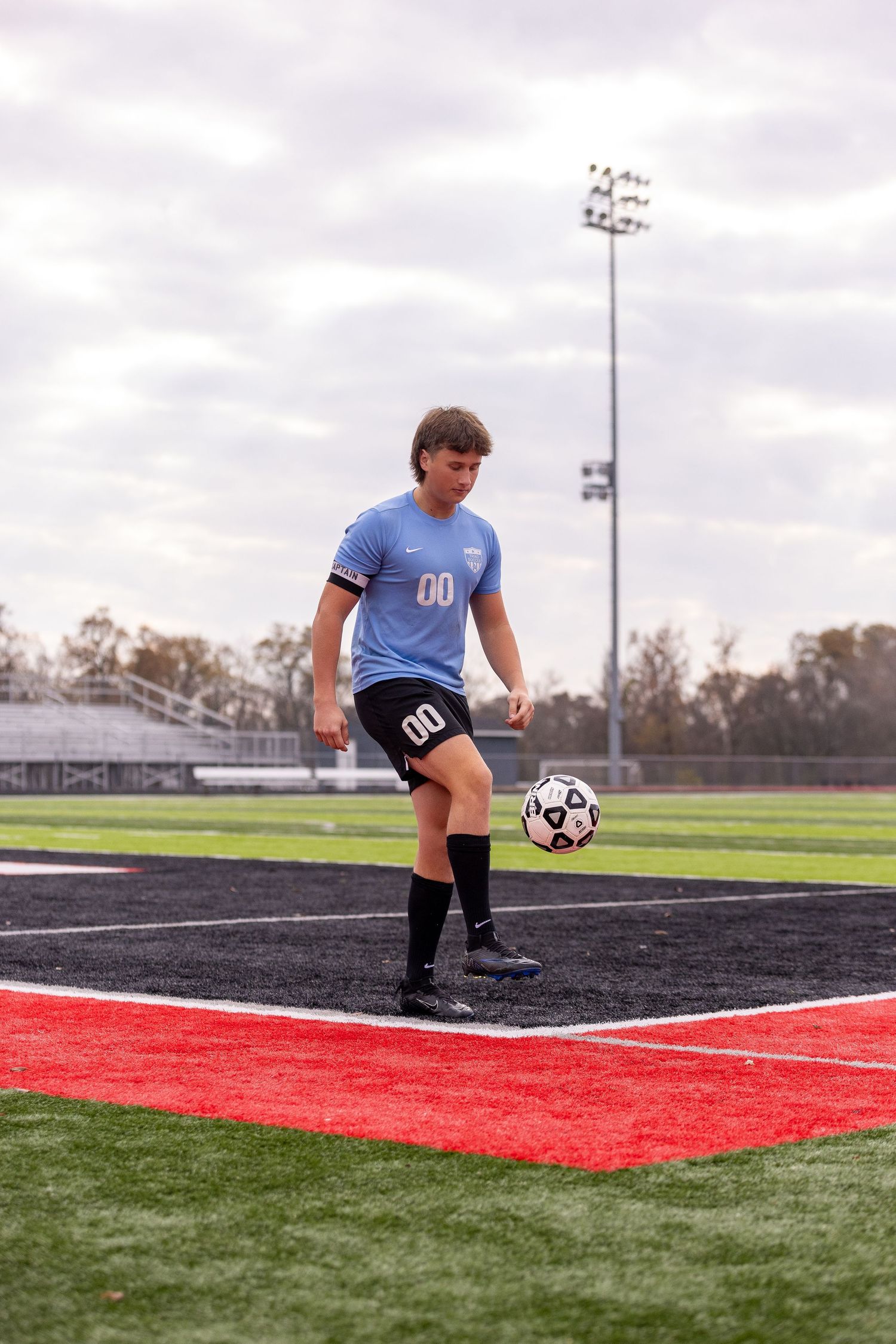 Soccer player in light blue jersey practicing ball control on sports field.