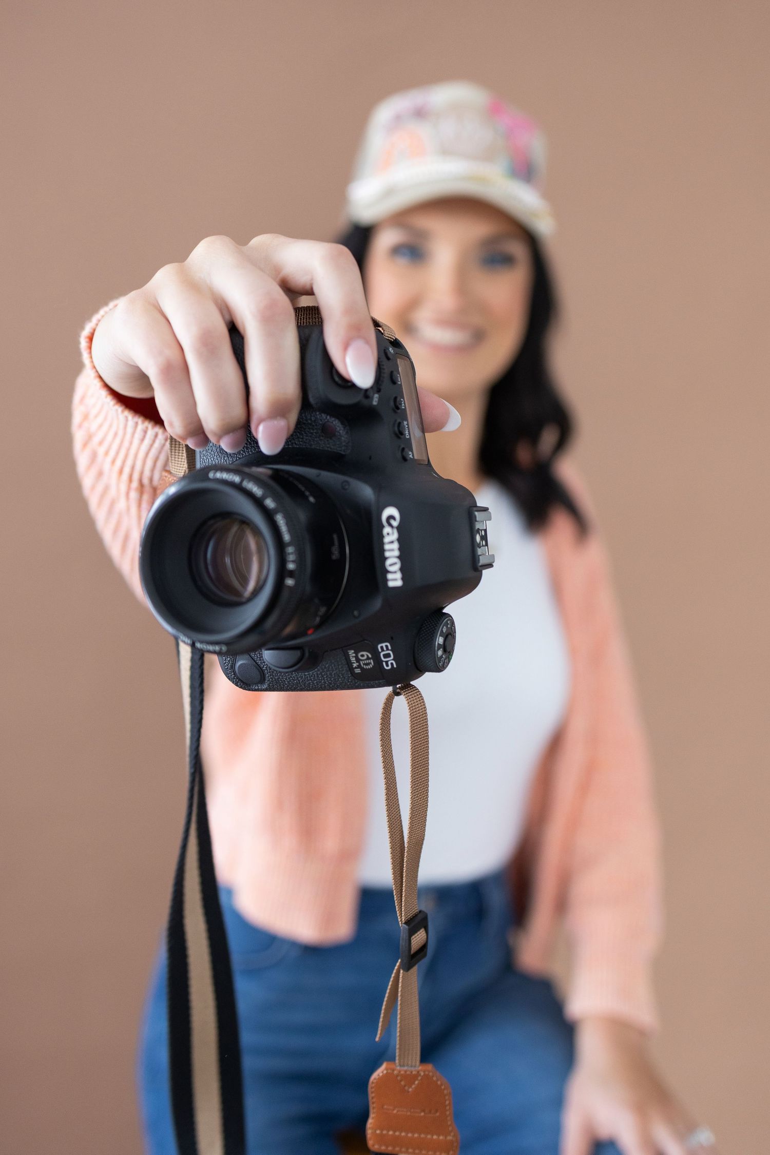 Person holding black Canon DSLR camera against peach colored background.