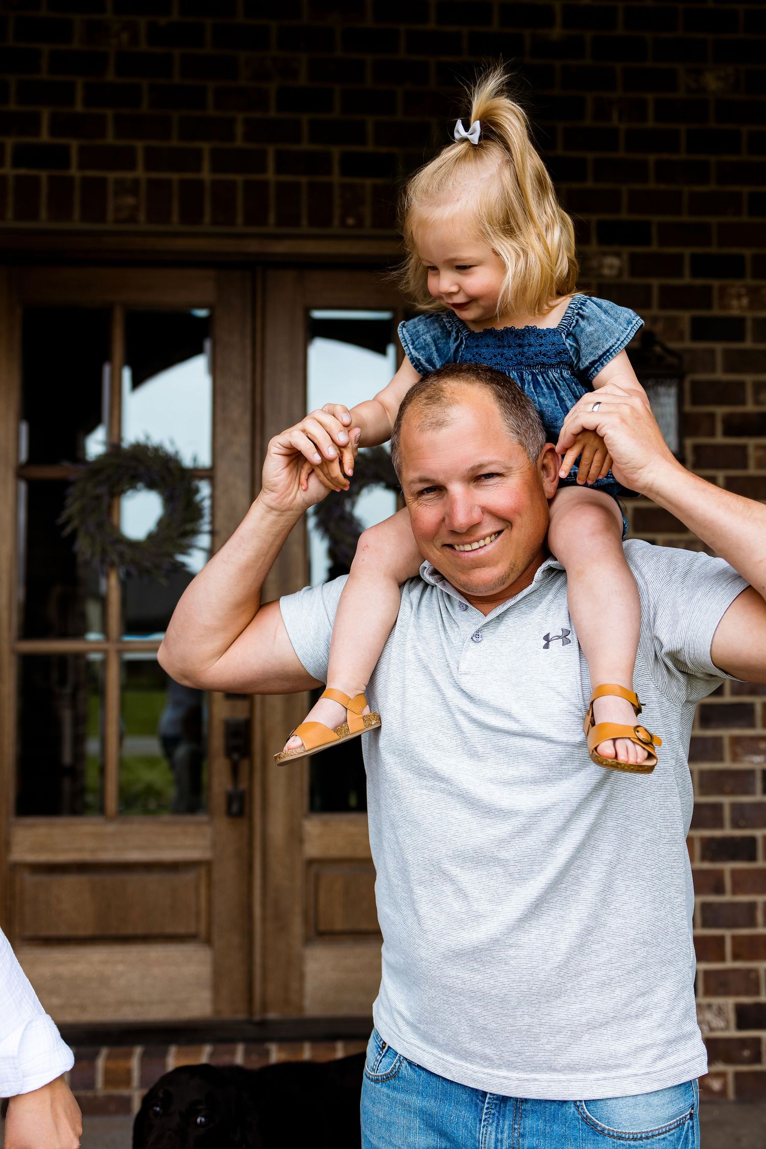 A playful shoulder ride moment captured against a brick building entrance.