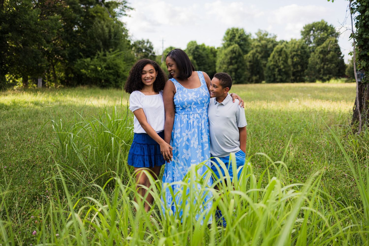 Family members share a joyful moment together in a sunlit meadow with tall green grass.