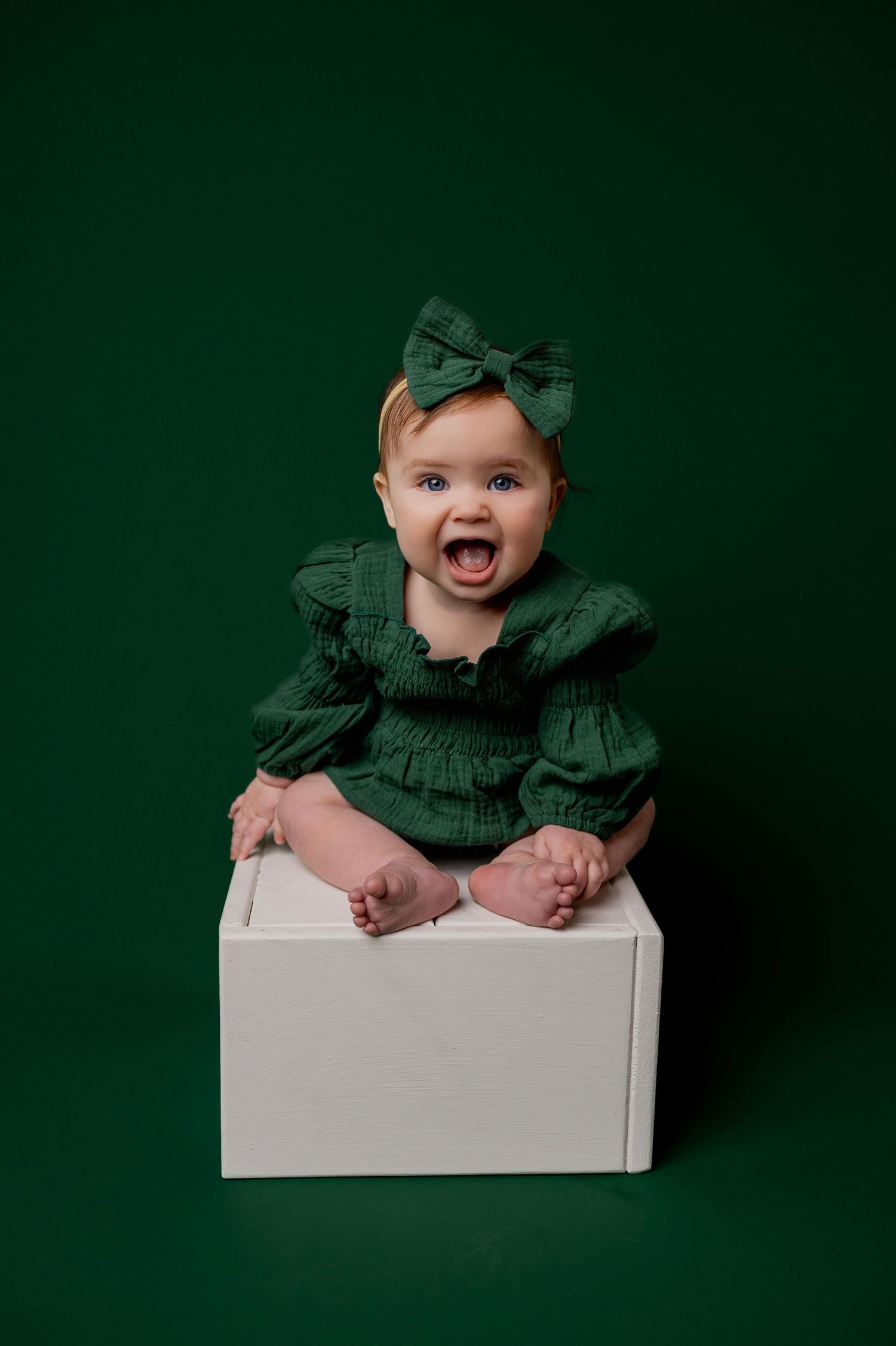 A sequence of four photos showing a baby in a green outfit sitting in a white box against a dark green background.