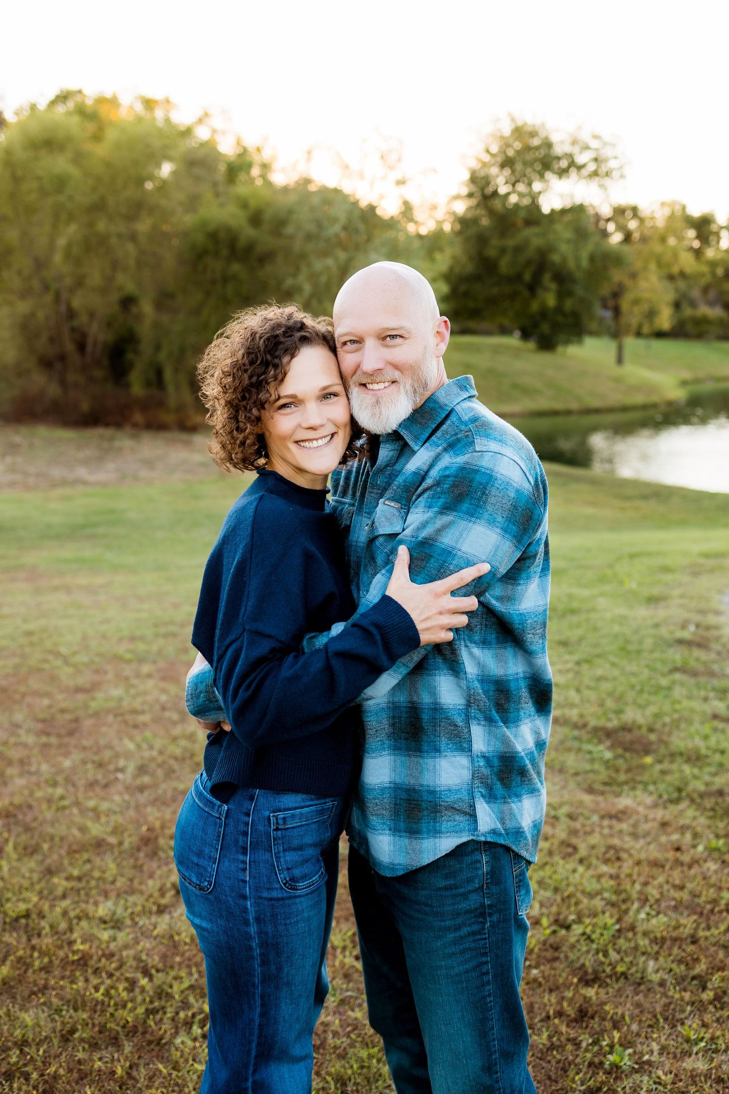 A couple shares joyful laughter while embracing outdoors in a grassy field at sunset.