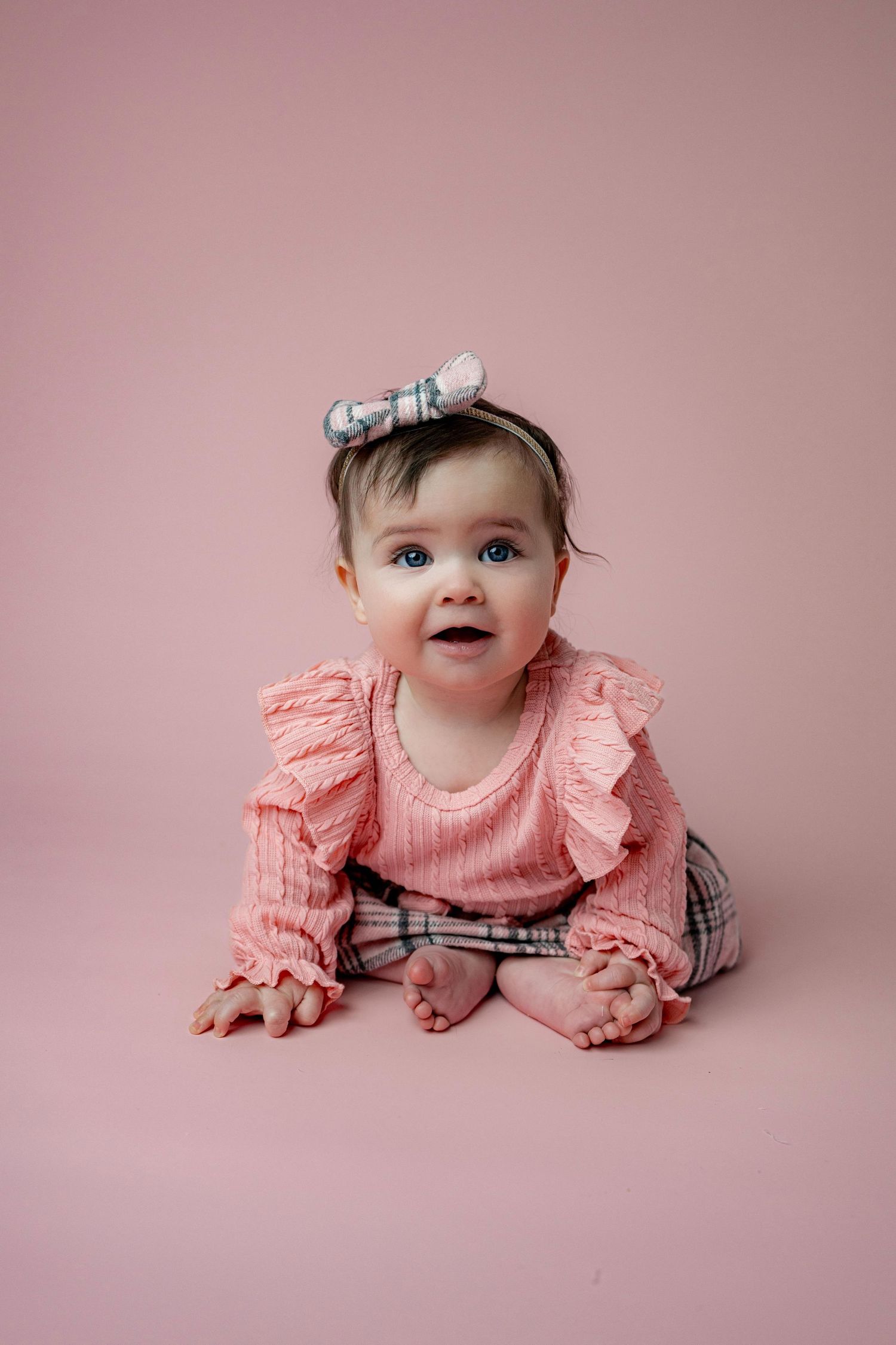 Sweet baby portrait on pink background wearing coral ruffled dress and hair bow.