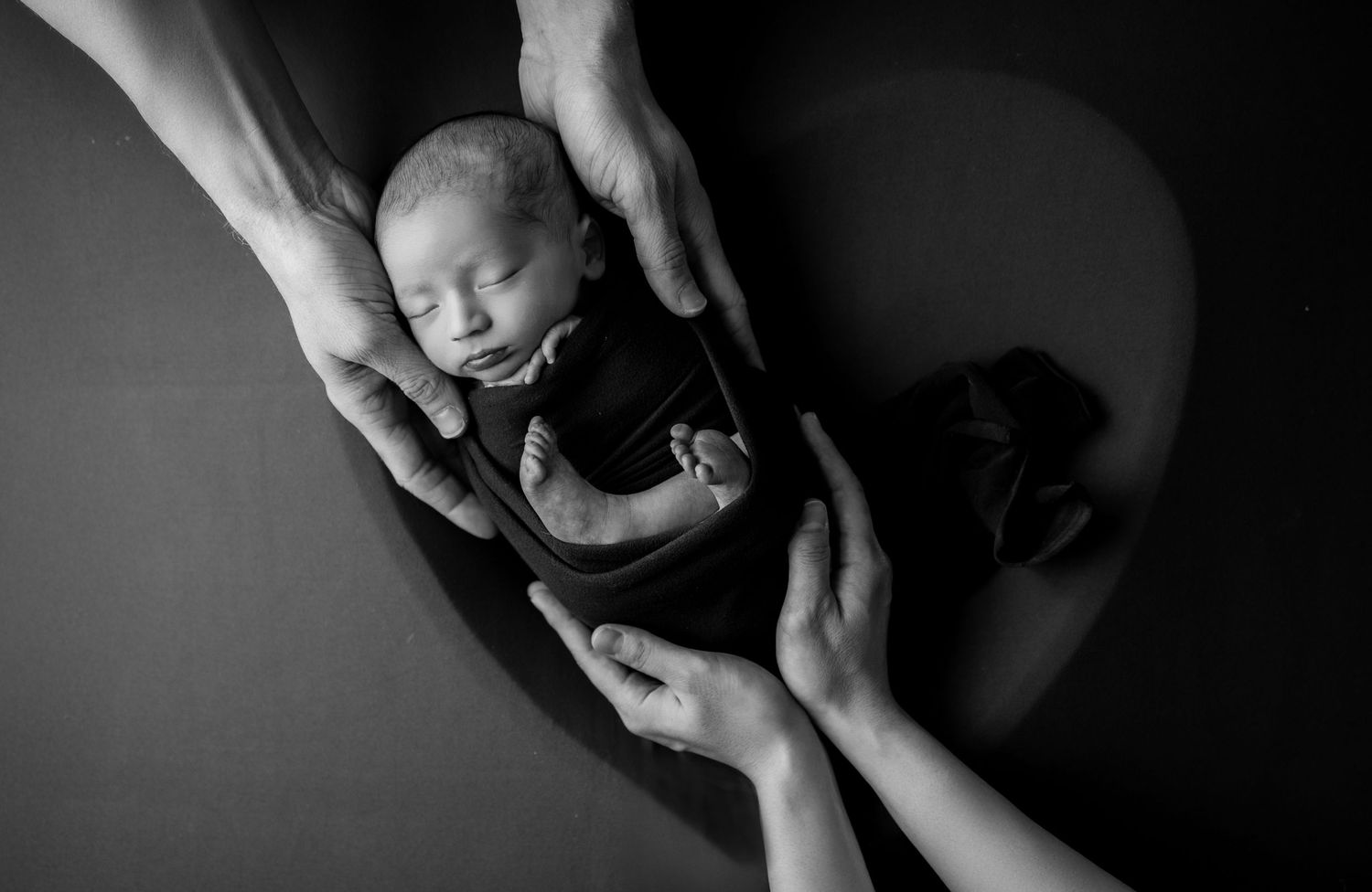 A dramatic black and white sequence showing hands cradling a small baby in different tender poses.