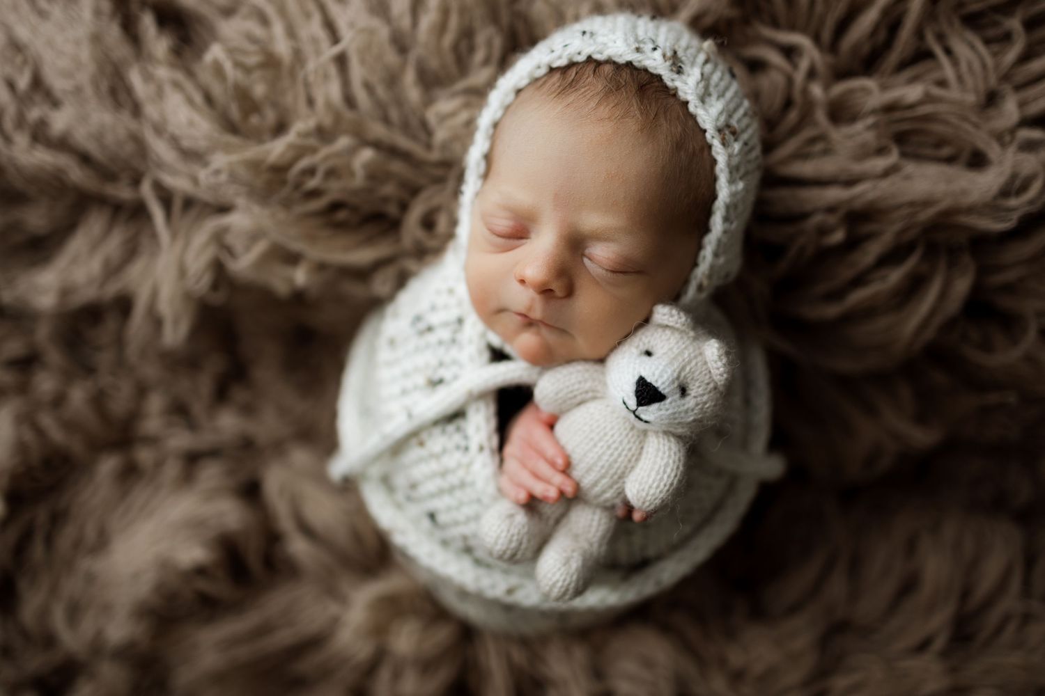 Collage of seven artistic newborn photos featuring a sleeping baby in white wraps and blankets on brown textured backgrounds.