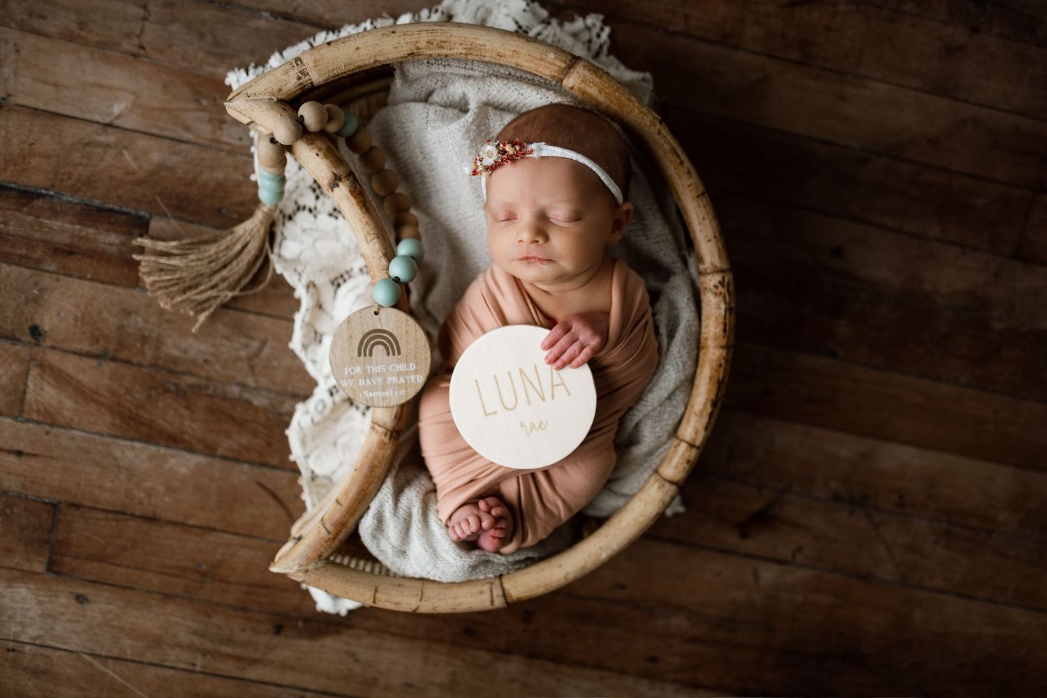Newborn baby sleeping peacefully in rustic wooden bowl with white floral accents and soft lighting.