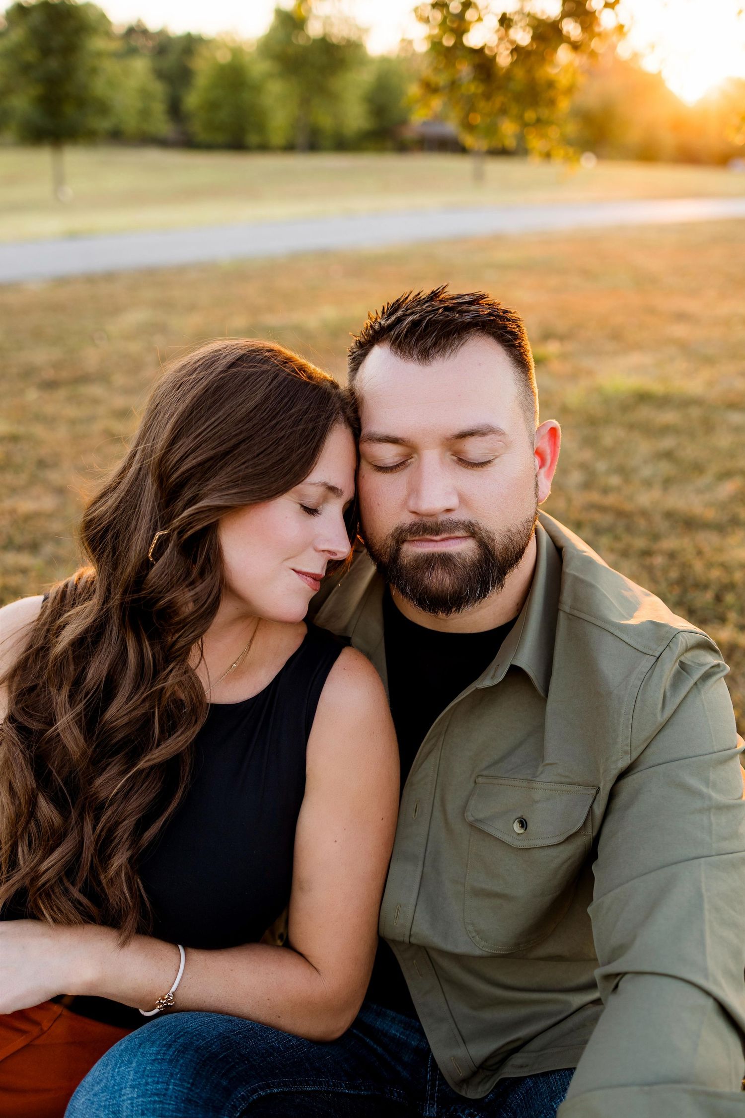 A couple shares intimate moments in a golden sunset field while sitting close together and embracing.