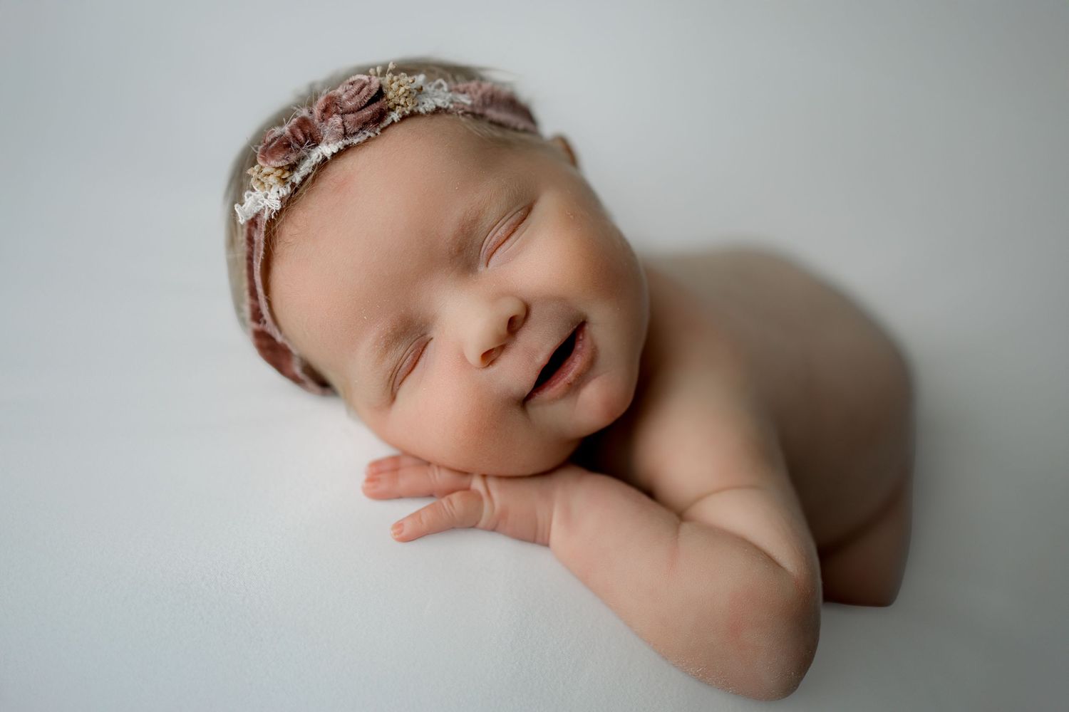 Peaceful sleeping newborn baby curled up in soft natural light during professional photography session.