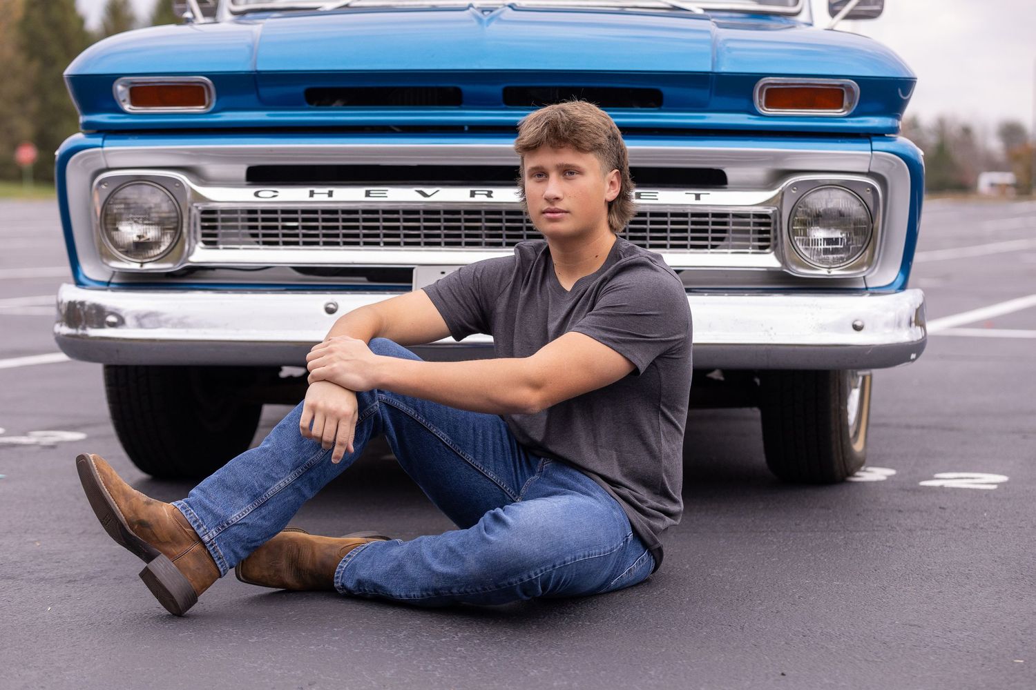 Person sitting on pavement in front of vintage blue Chevrolet truck.