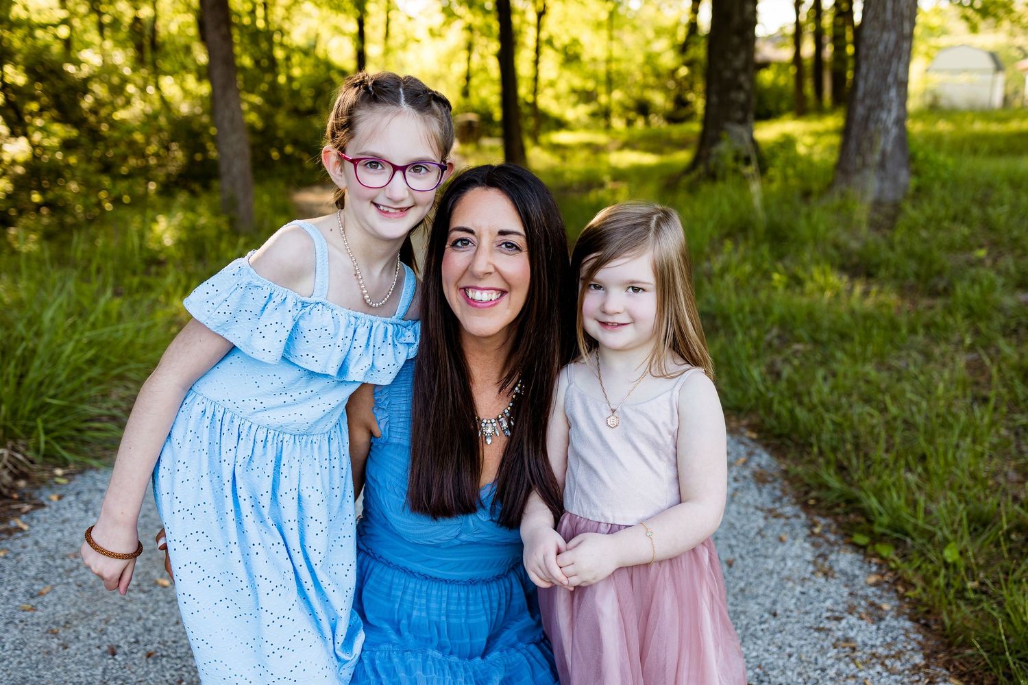 A heartwarming outdoor portrait in nature with matching dresses and smiles on a gravel path.