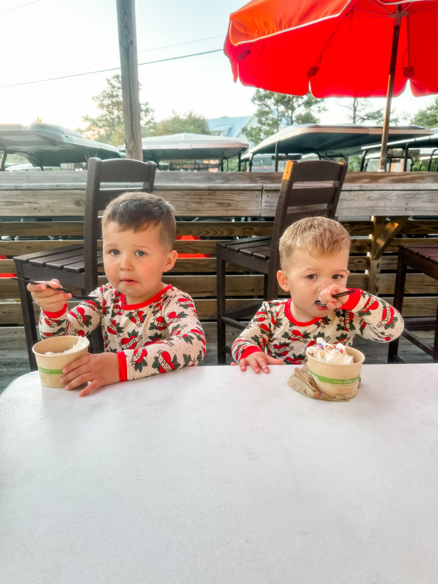 Two children in matching holiday sweaters enjoying desserts at outdoor restaurant table.