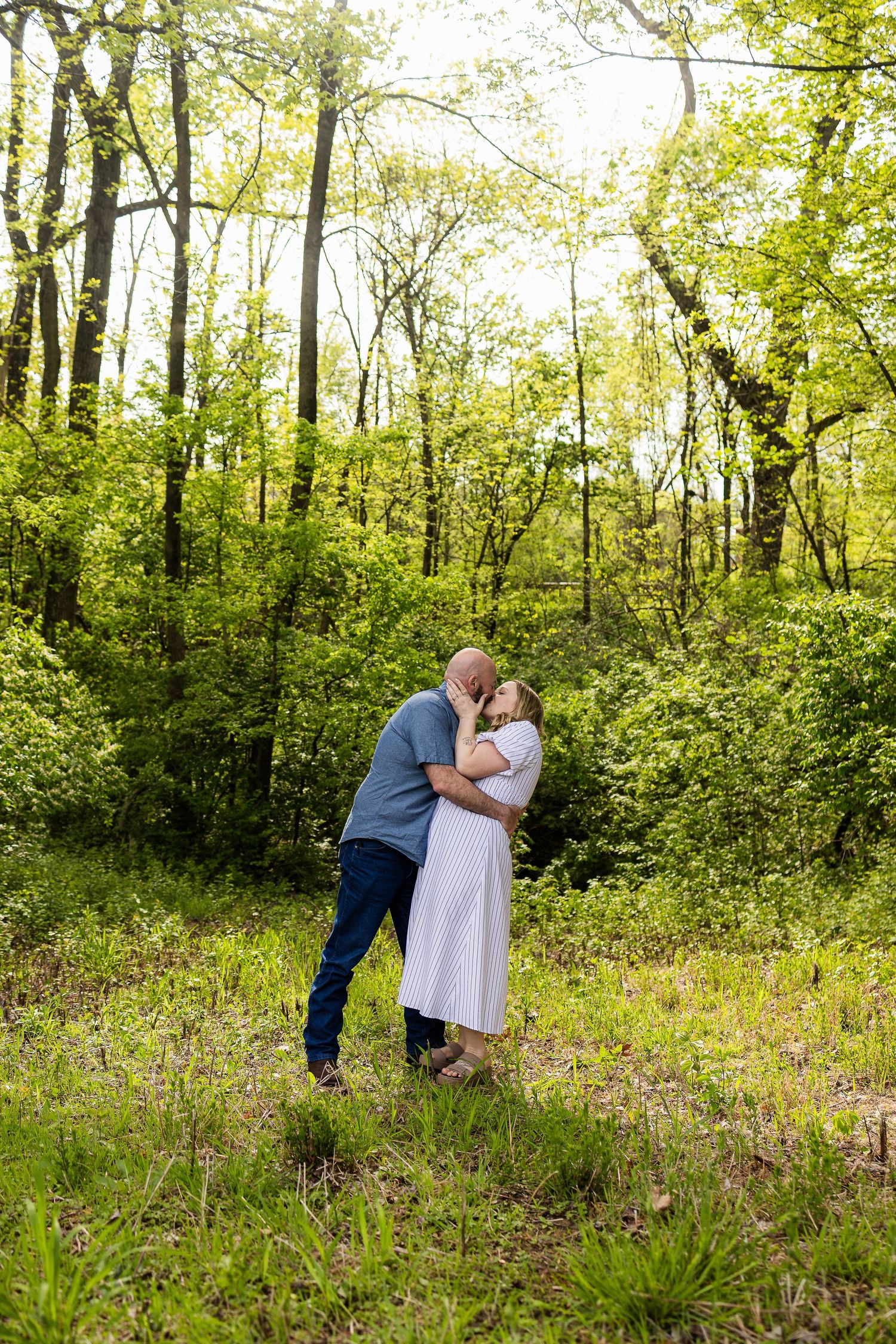Couple sharing romantic moment in sunlit forest clearing.