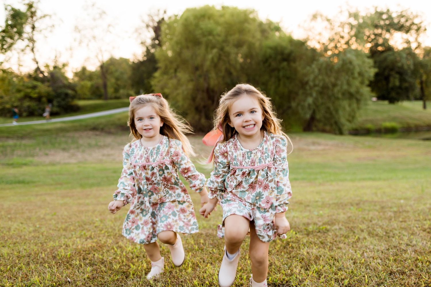 Children in floral dresses run and play together in a grassy field during golden hour.