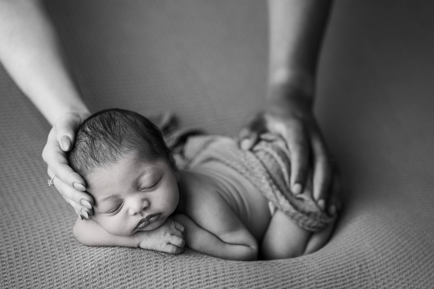 Professional black and white portrait of a peaceful sleeping newborn baby being gently cradled by adult hands.