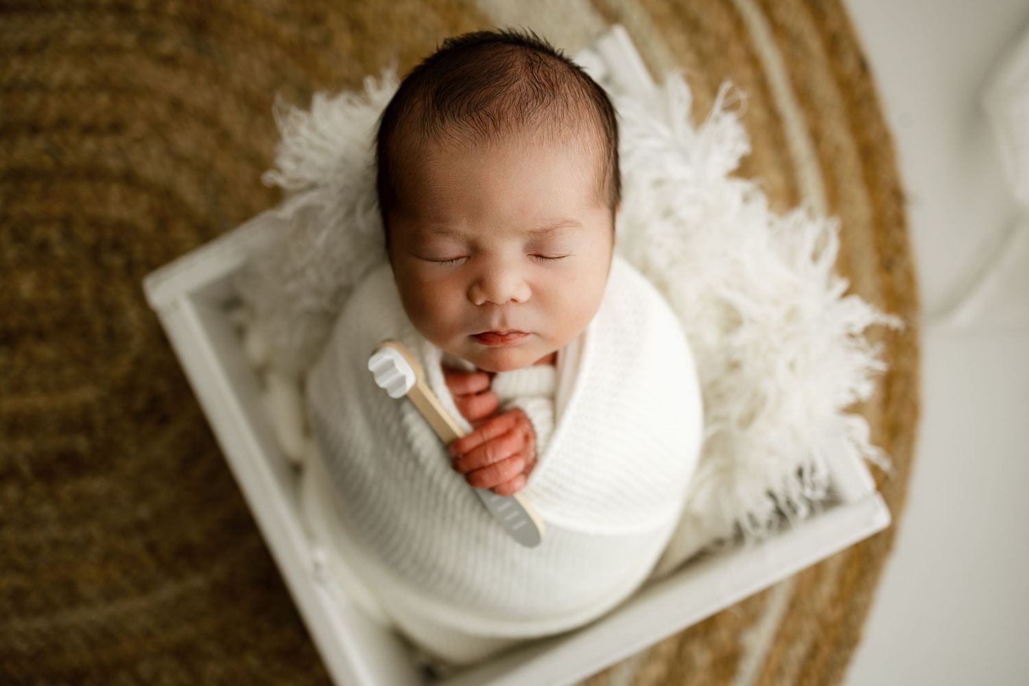 A newborn baby wrapped in white swaddle cloth sleeps peacefully on a beige textured background.